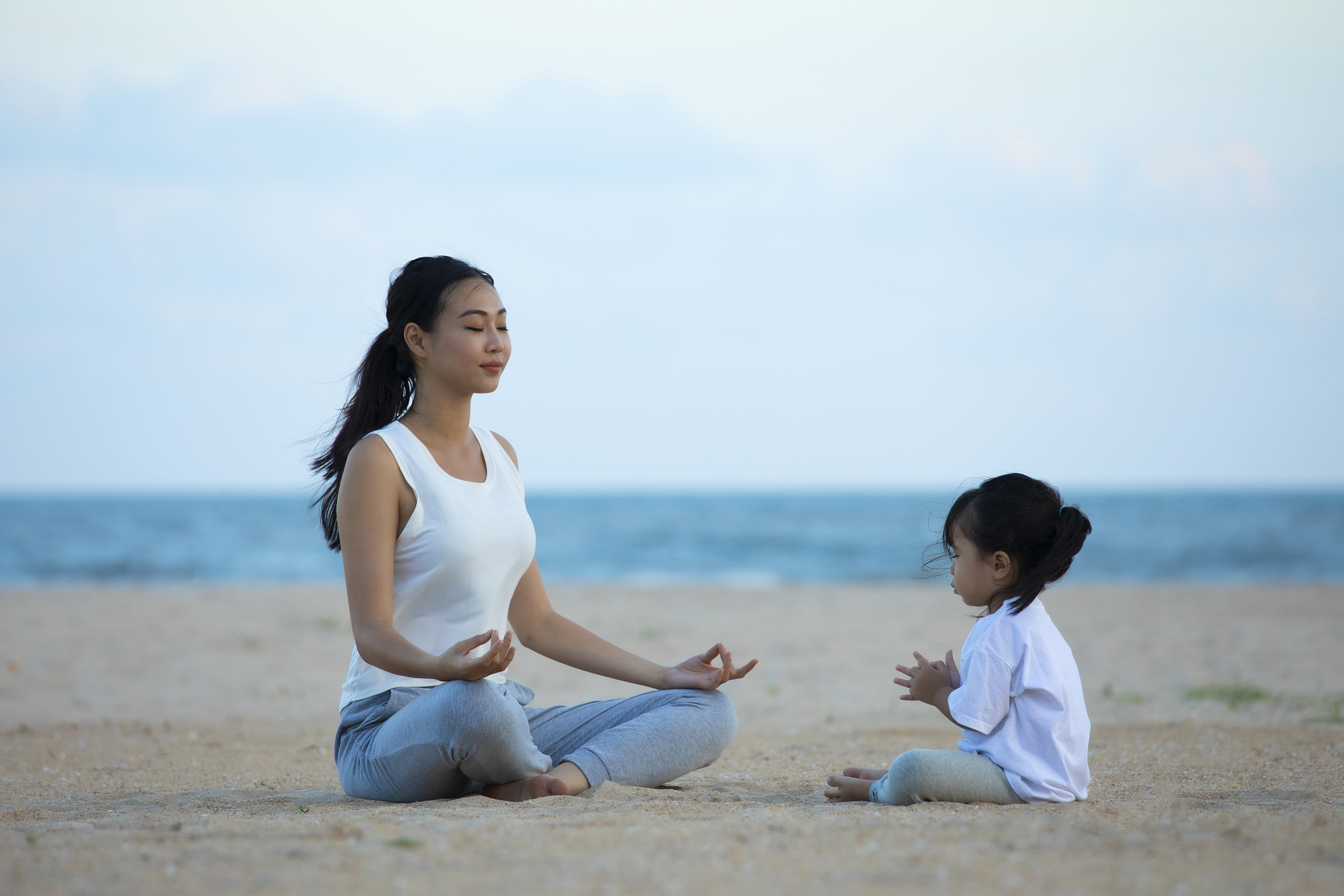 Asian mother and child meditating on a serene sandy beach.