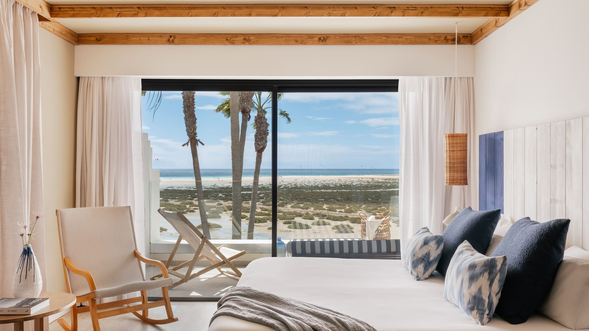Coastal bedroom with ocean view, palm trees, and modern king bed.