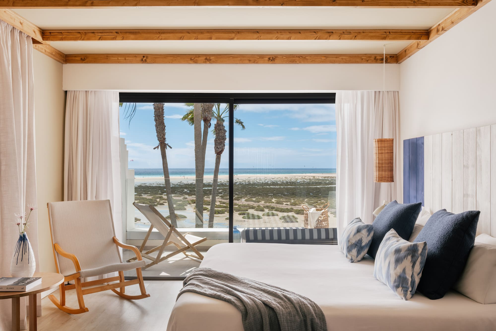 Coastal bedroom with ocean view, palm trees, and modern king bed.