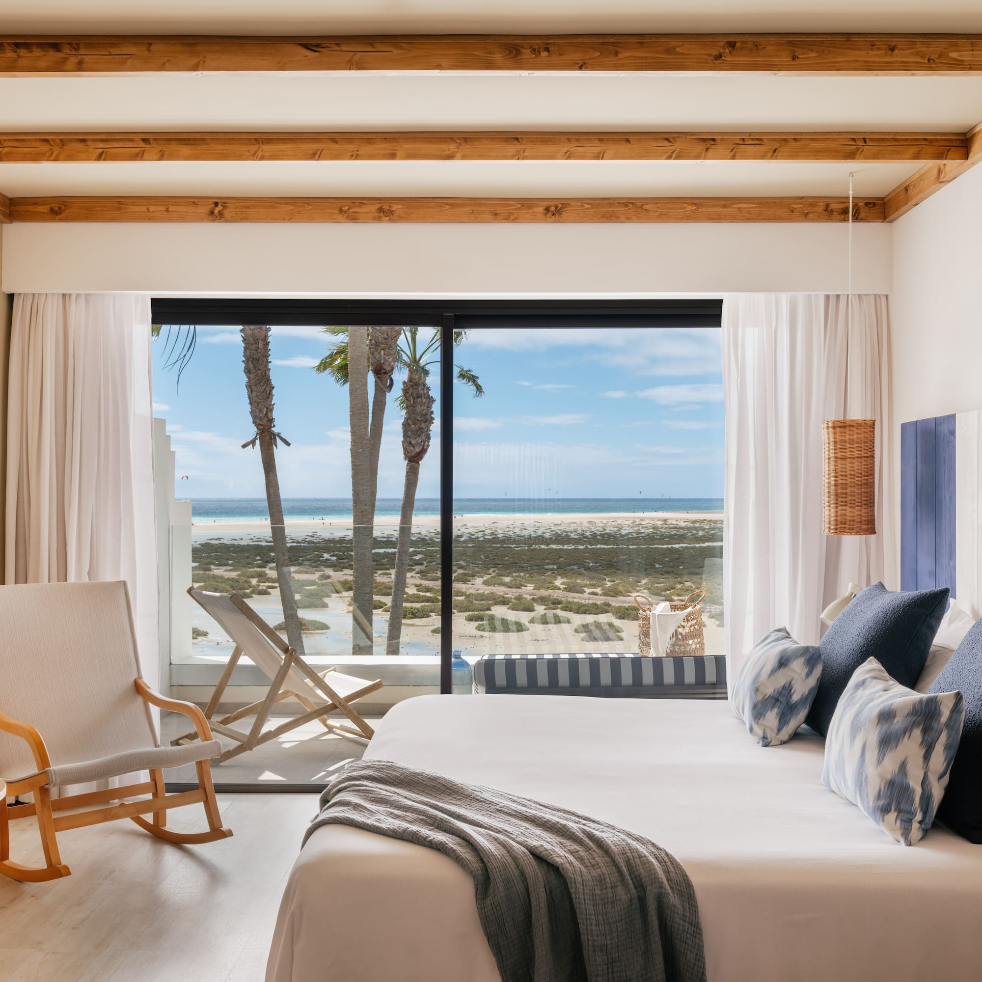 Coastal bedroom with ocean view, palm trees, and modern king bed.