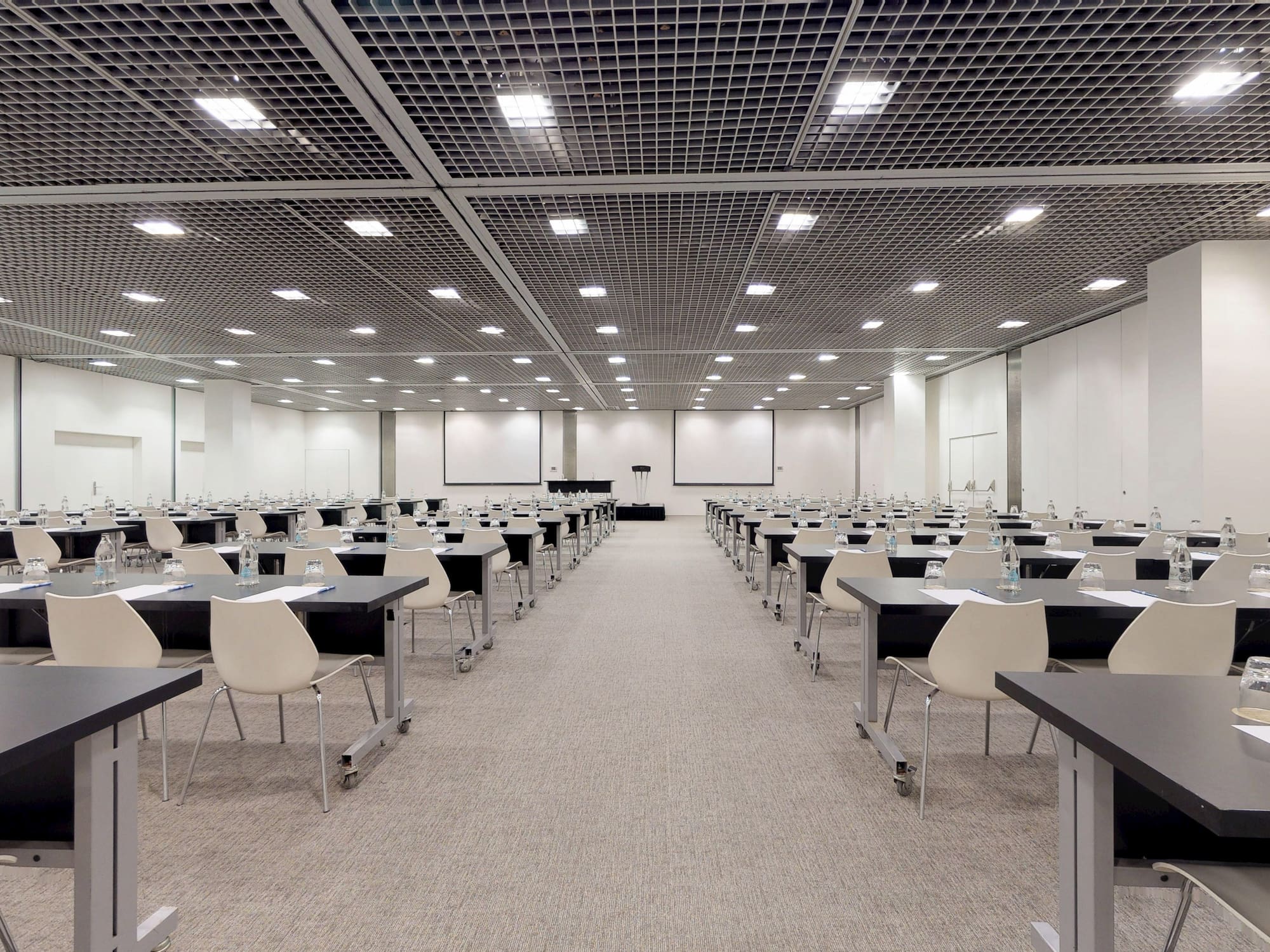 Modern conference venue with tables, chairs, and screens ready for an event.