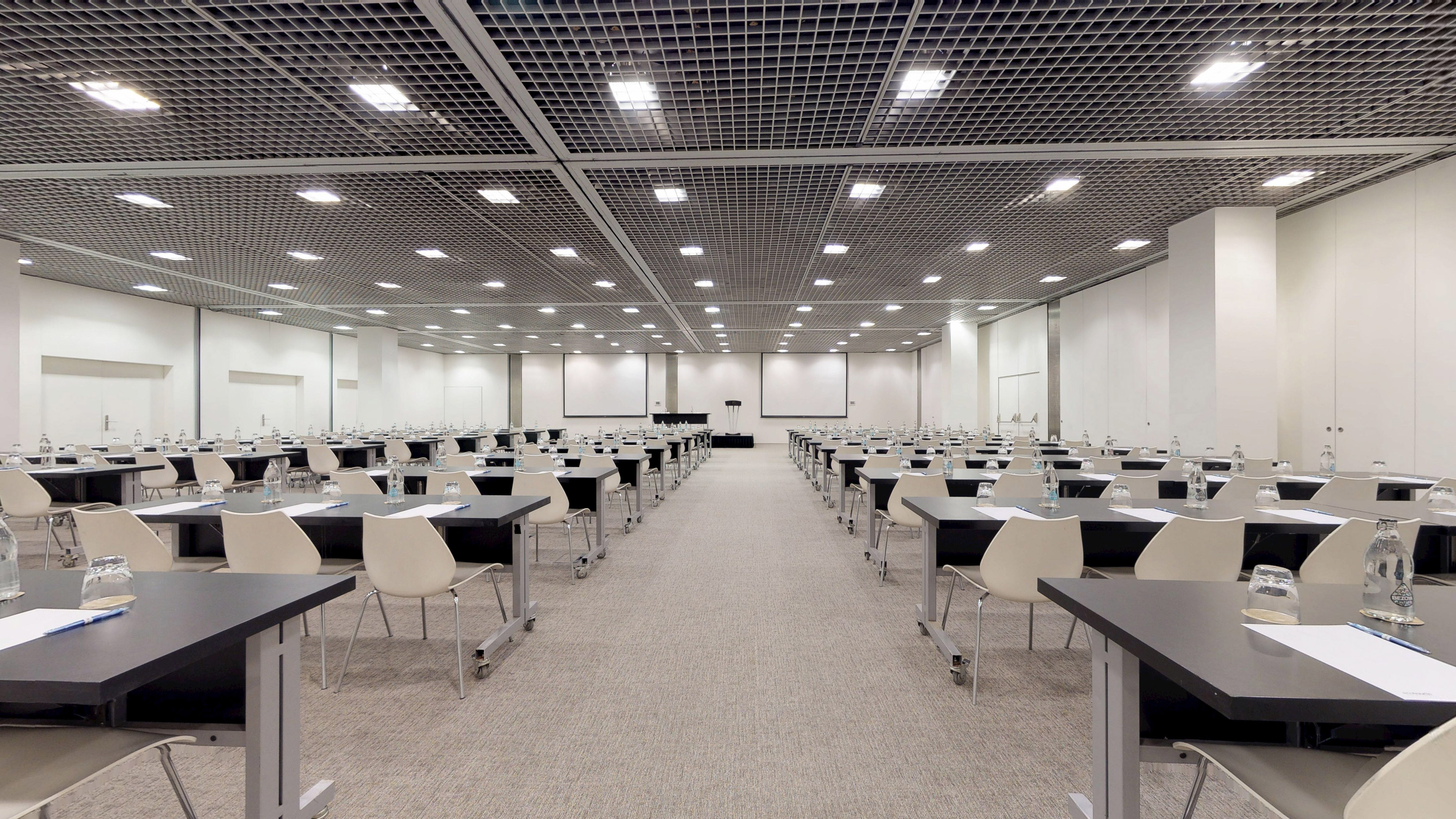 Modern conference venue with tables, chairs, and screens ready for an event.
