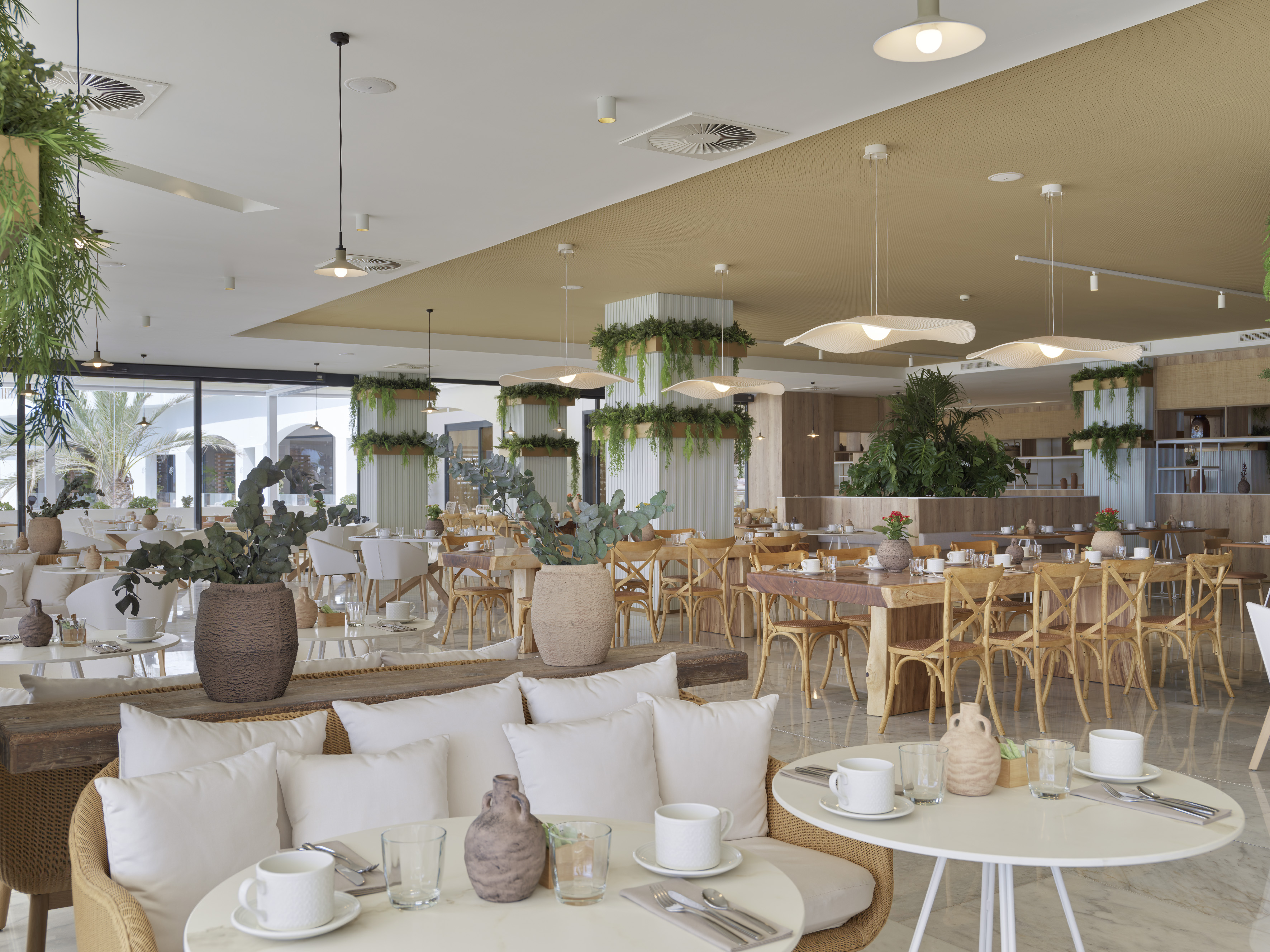 Modern restaurant interior with light wood, rattan seating, and lush green plants.