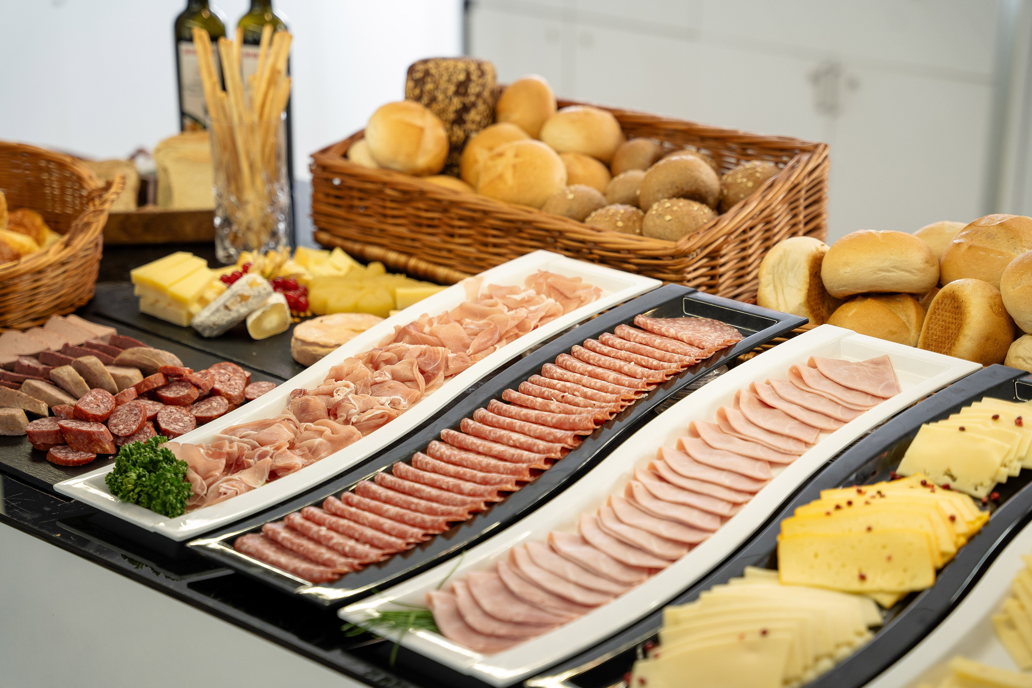 Deli buffet with cold cuts, assorted cheeses, and fresh baked bread rolls.