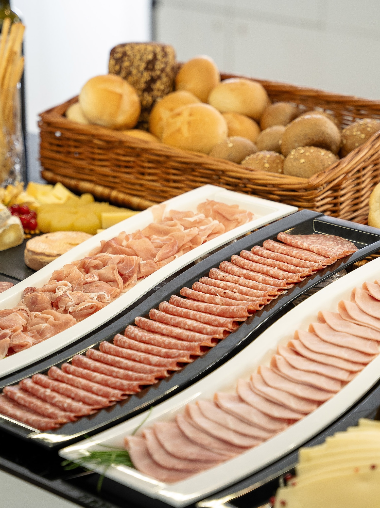 Deli buffet with cold cuts, assorted cheeses, and fresh baked bread rolls.