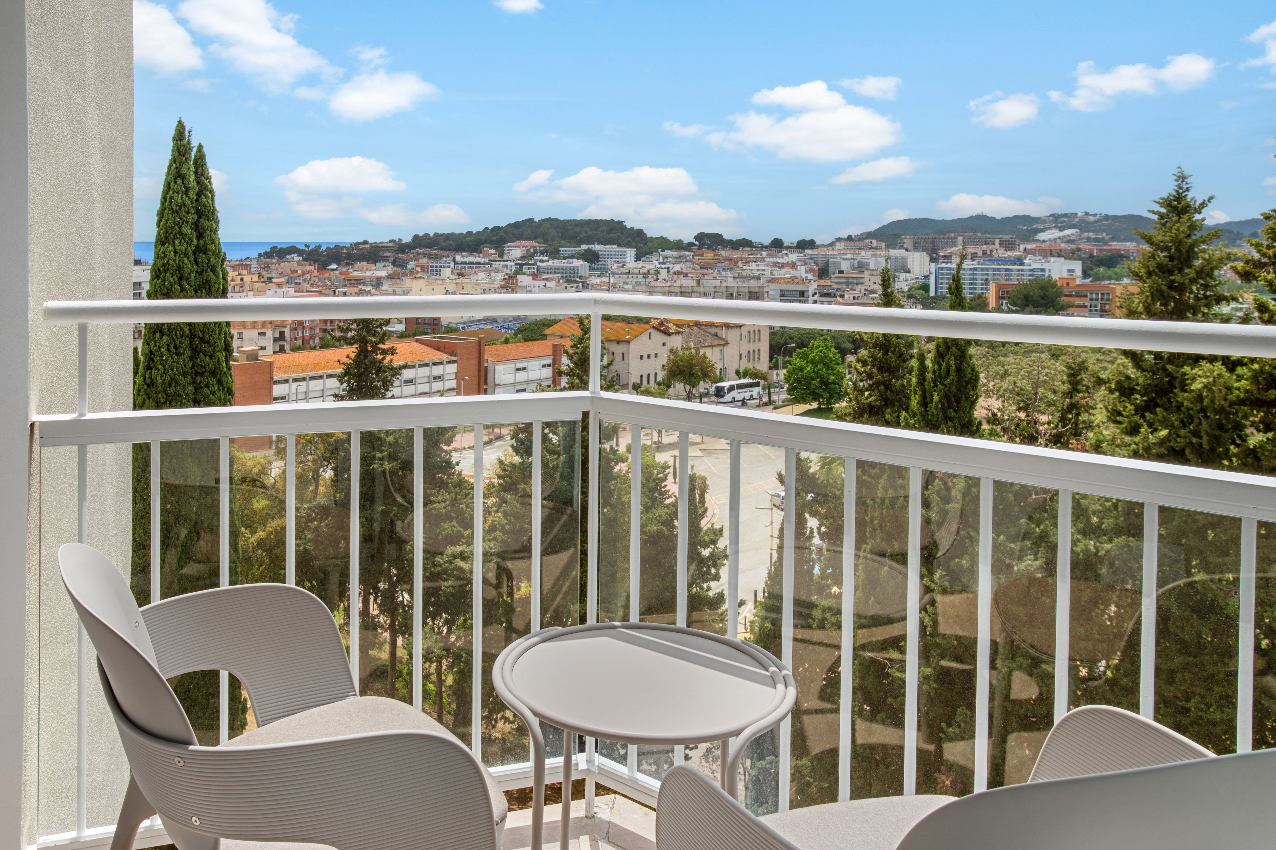 Hotel balcony with grey chairs, table, coastal city, and ocean view.