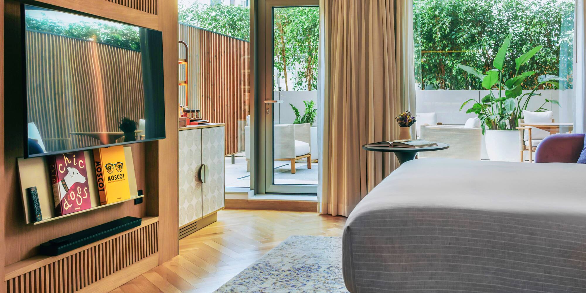 Modern hotel bedroom, wooden TV wall, herringbone floor, green patio.