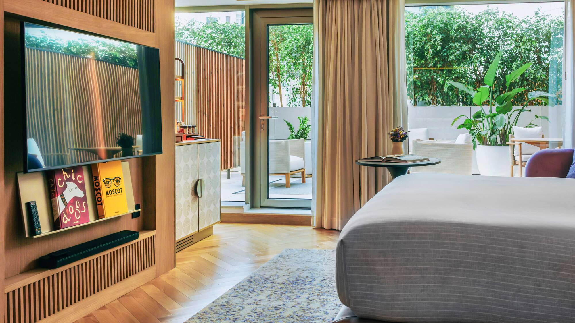 Modern hotel bedroom, wooden TV wall, herringbone floor, green patio.