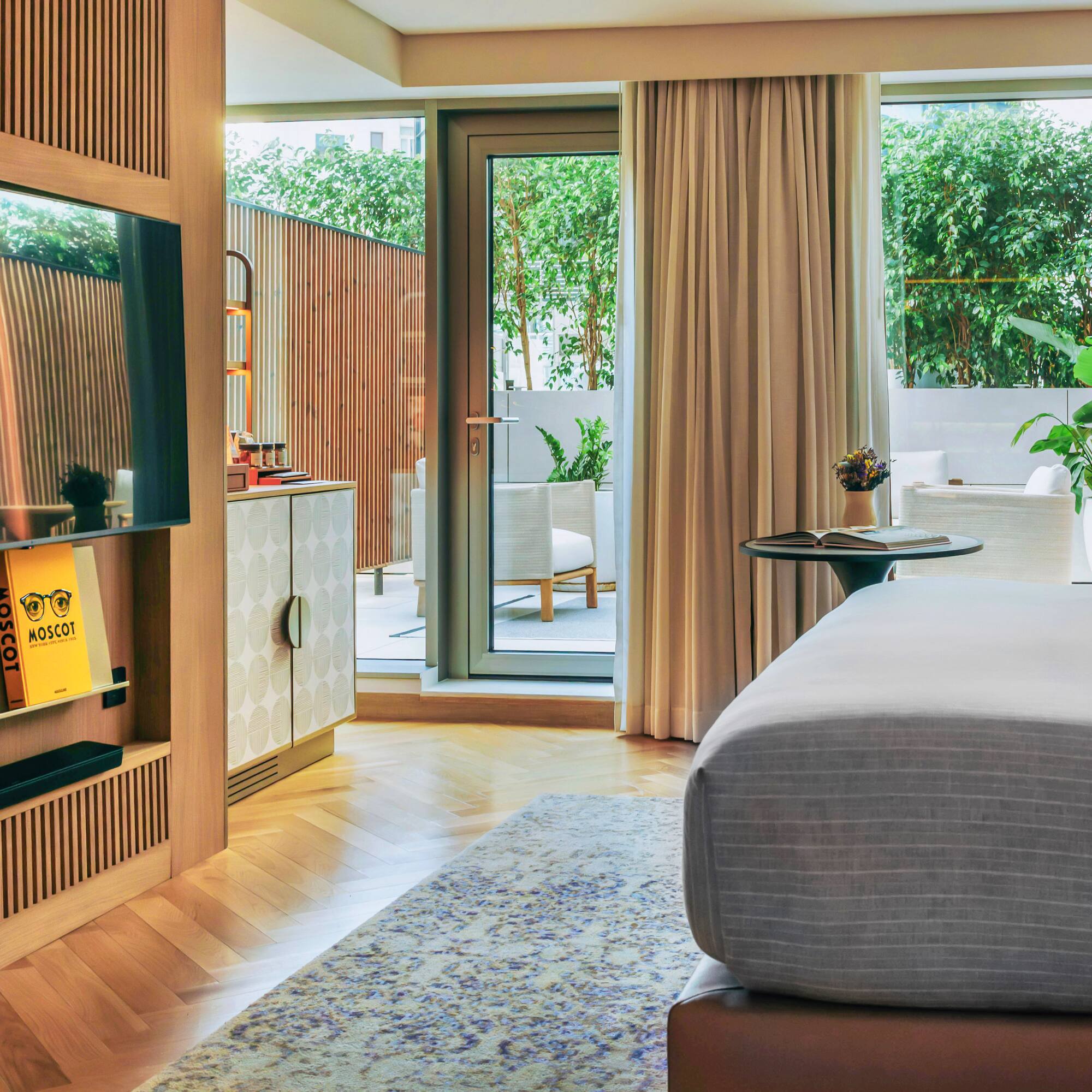 Modern hotel bedroom, wooden TV wall, herringbone floor, green patio.