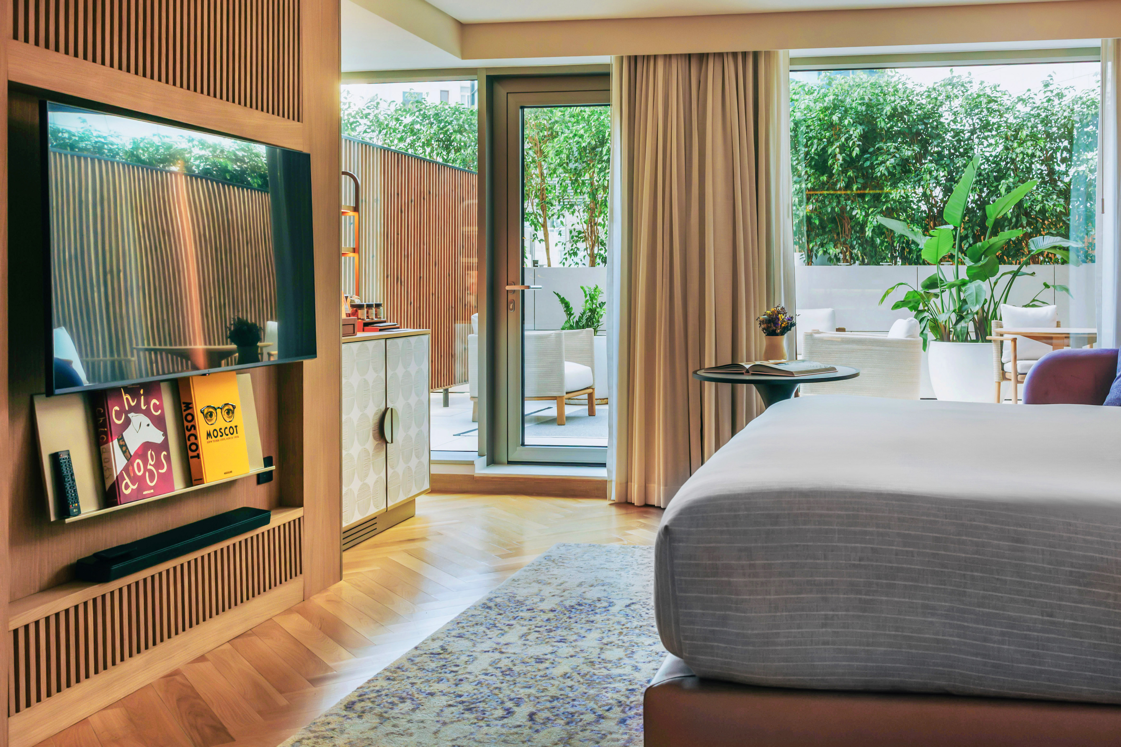 Modern hotel bedroom, wooden TV wall, herringbone floor, green patio.