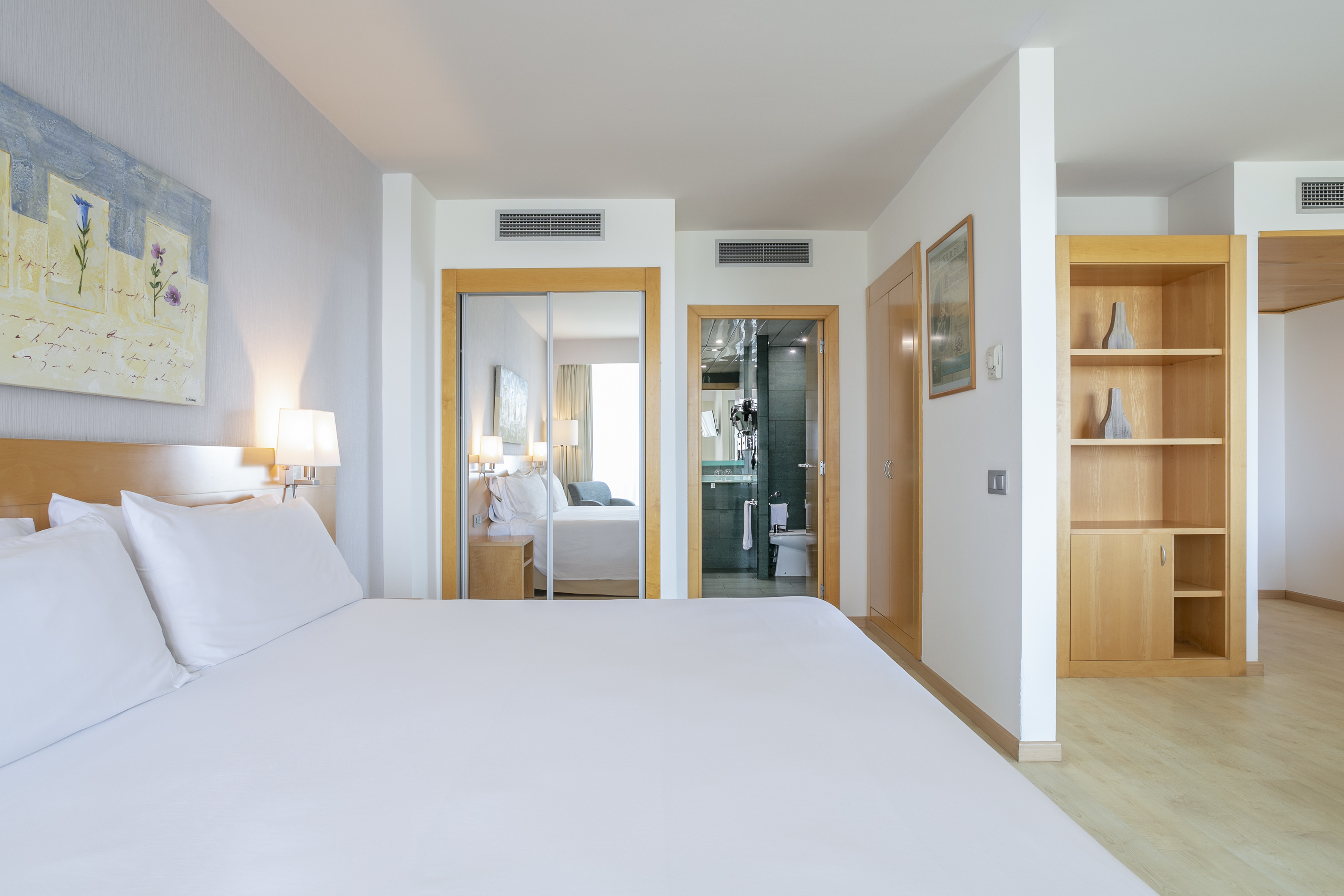Modern hotel bedroom with white bed, mirrored wardrobe, and integrated bathroom.