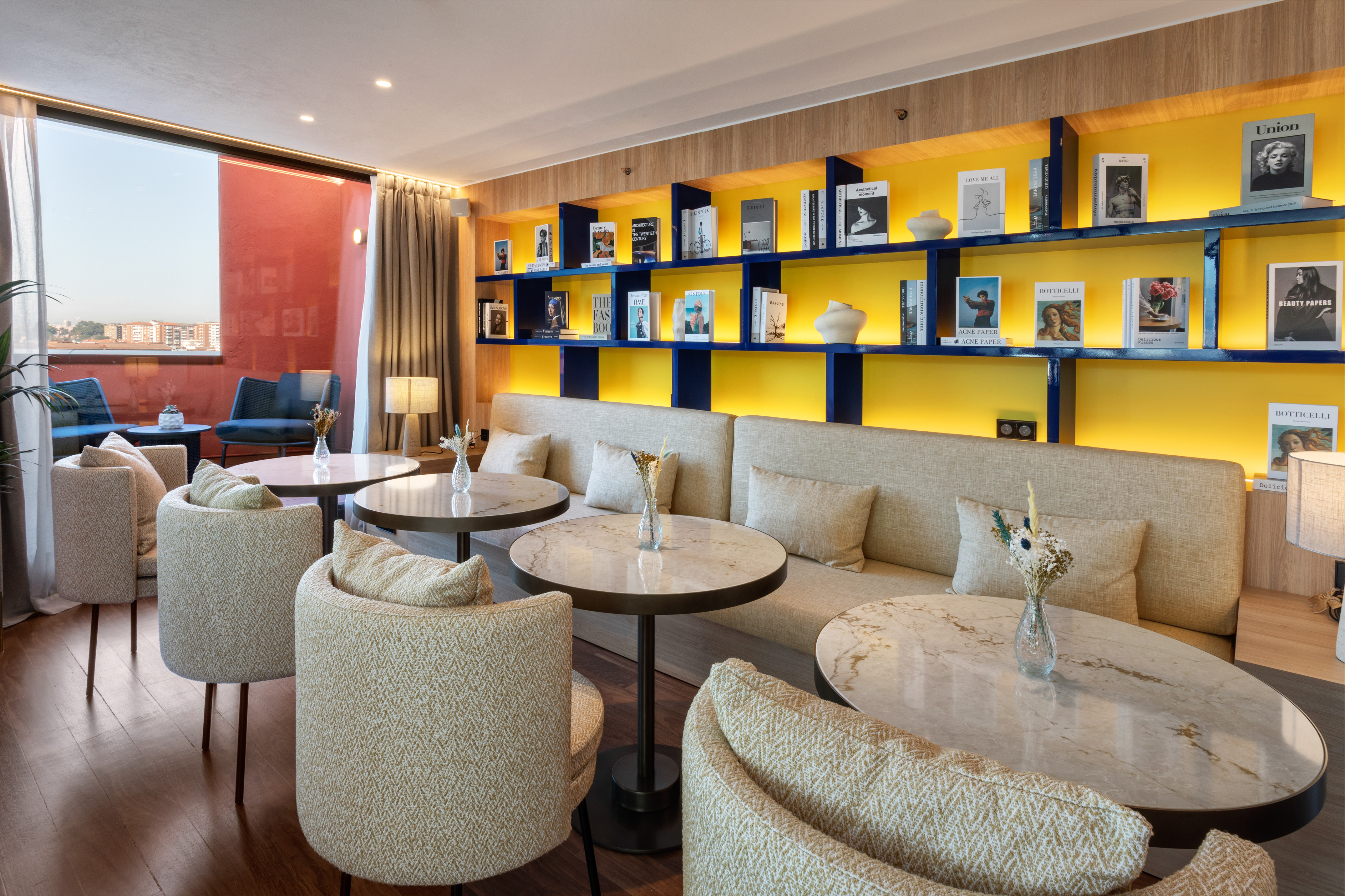 Contemporary lounge with vibrant yellow bookshelf, comfy seating, marble tables.