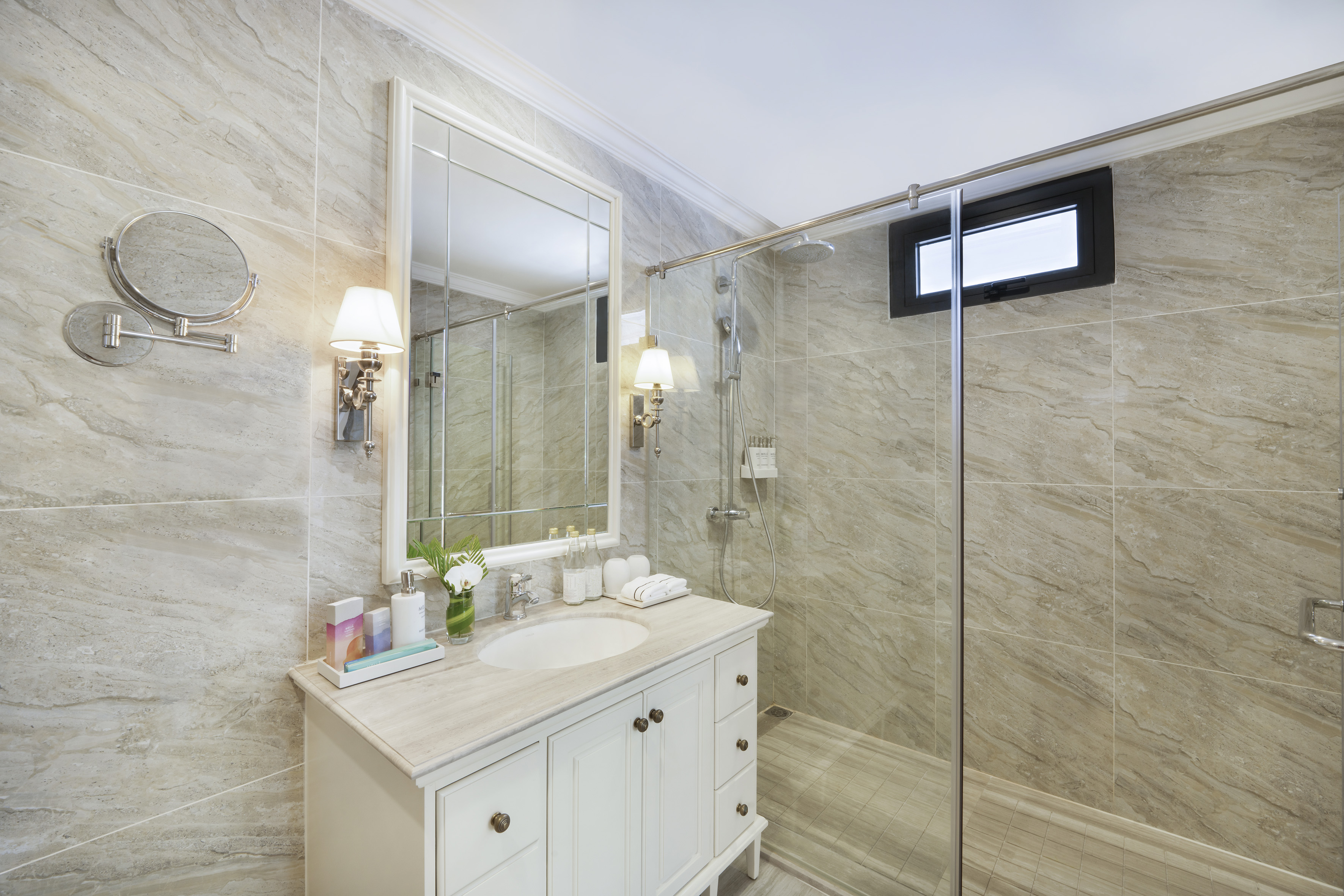 Modern marble bathroom with white vanity, large mirror, and glass walk-in shower.