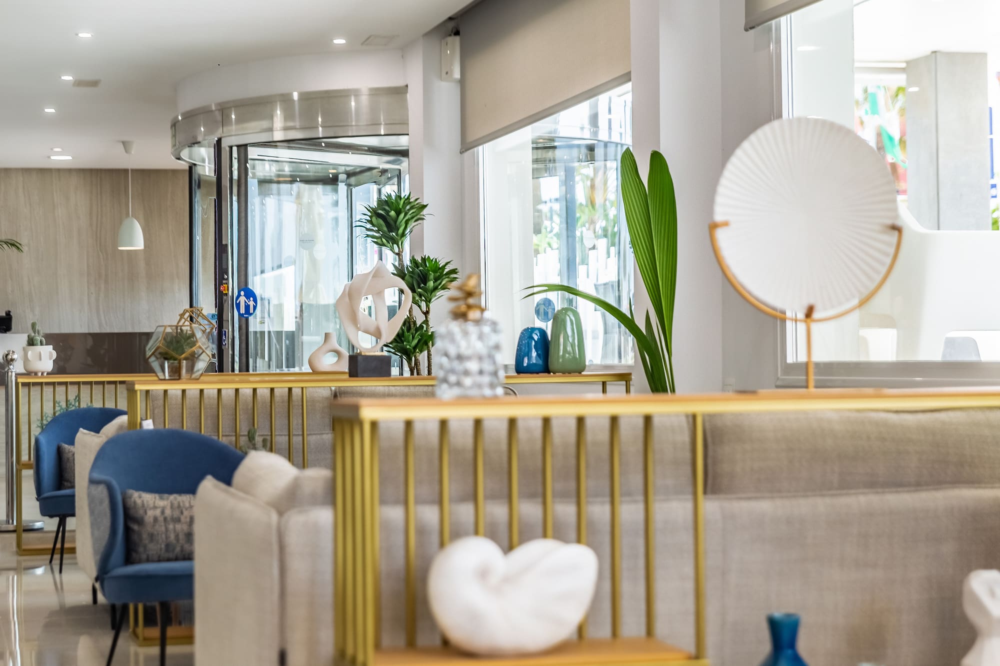 Modern hotel lobby with comfortable seating, decorative plants, and revolving door.