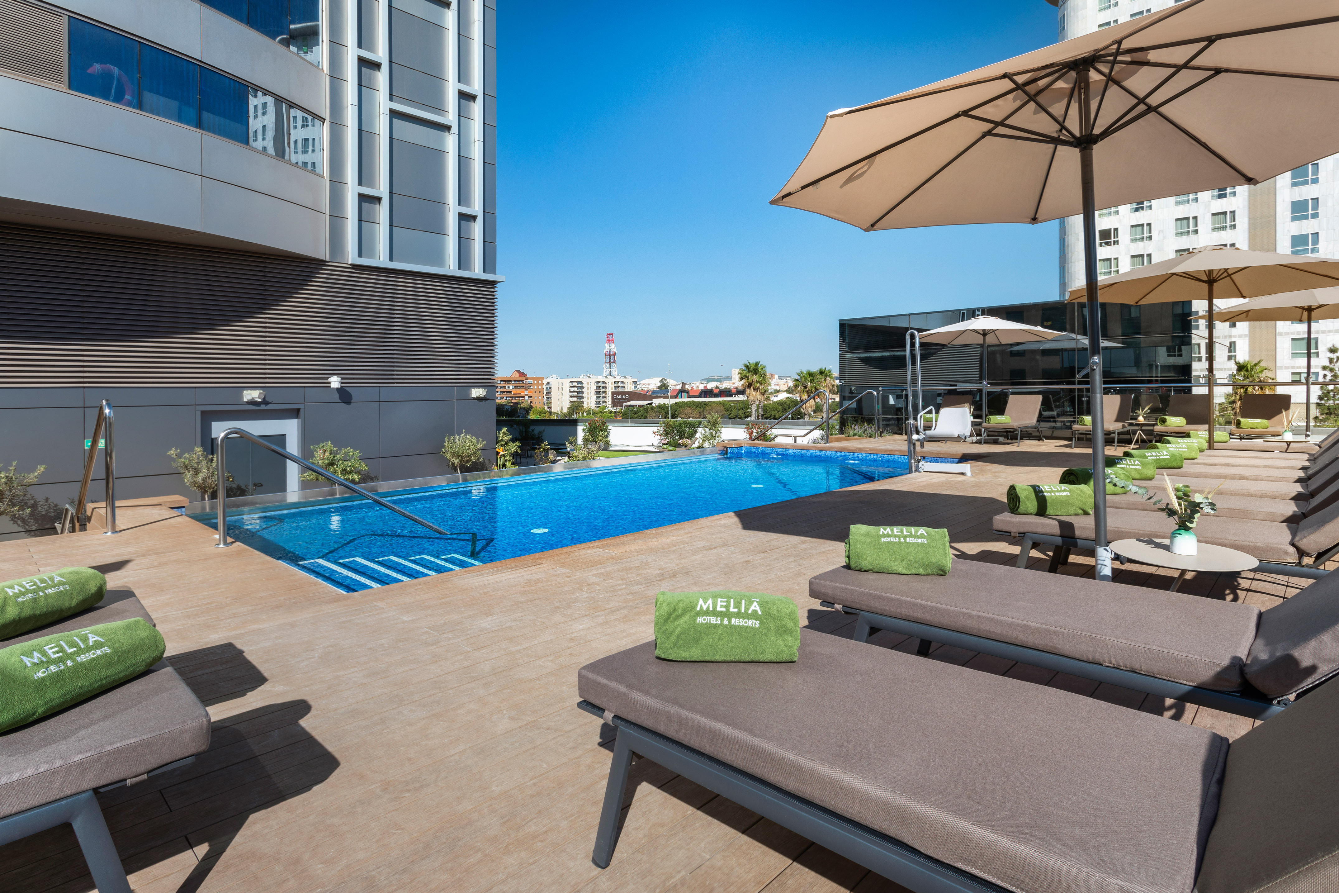 Modern Melia hotel rooftop pool with sun loungers, umbrellas, and city views.