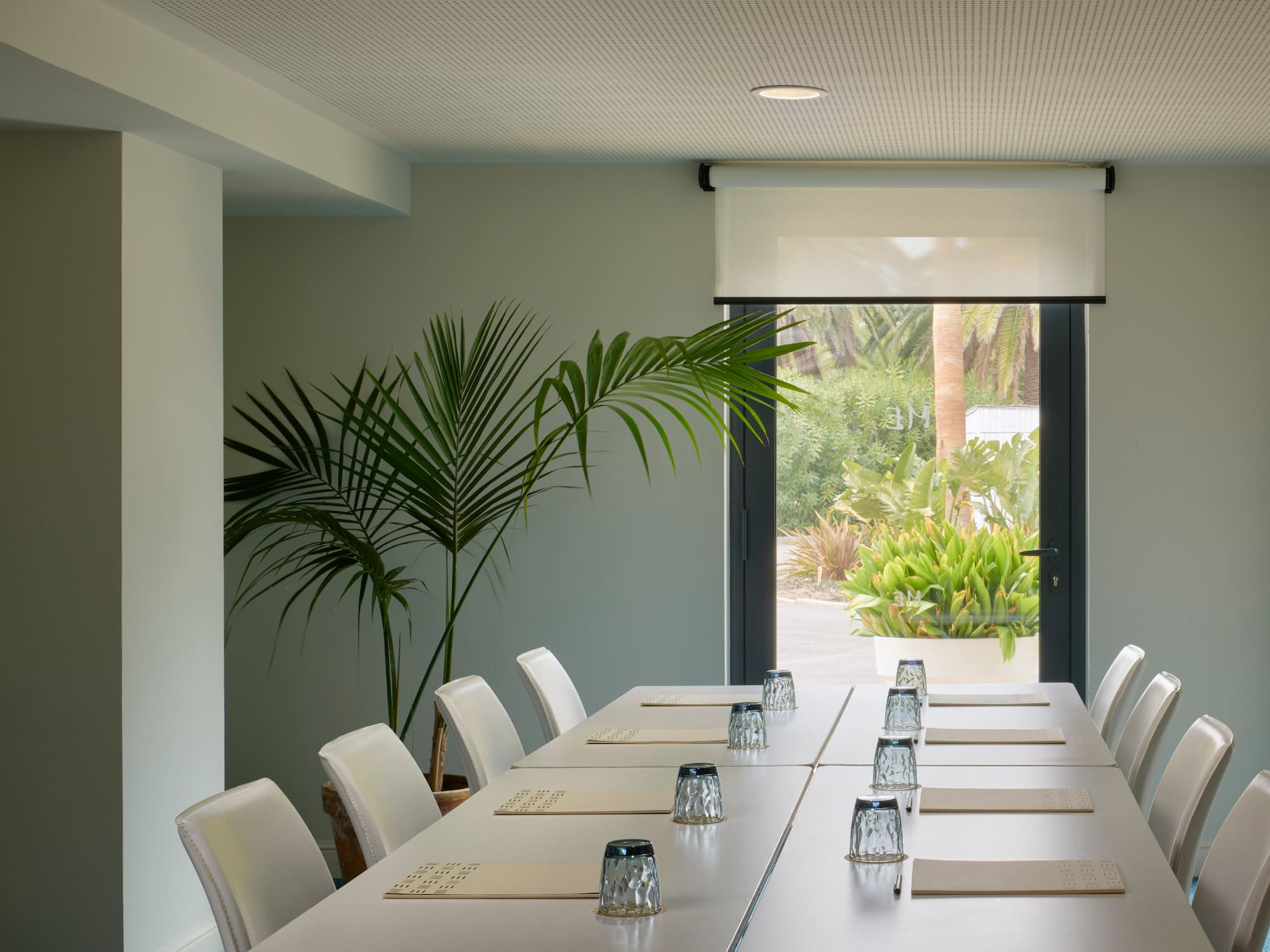 a long table with white chairs and glasses on it.