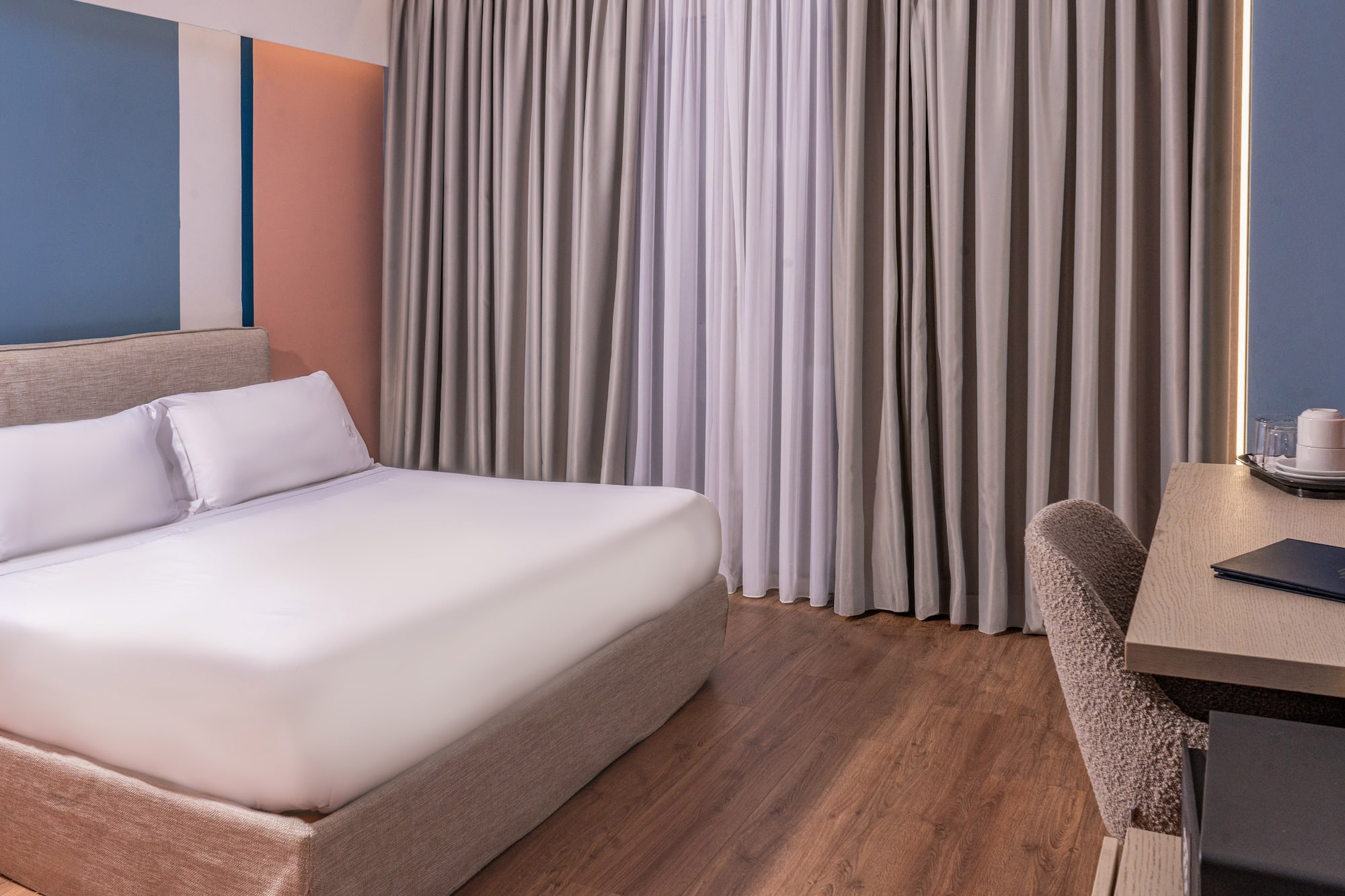 Modern hotel room with king bed, color-block wall, hardwood floor, and desk.