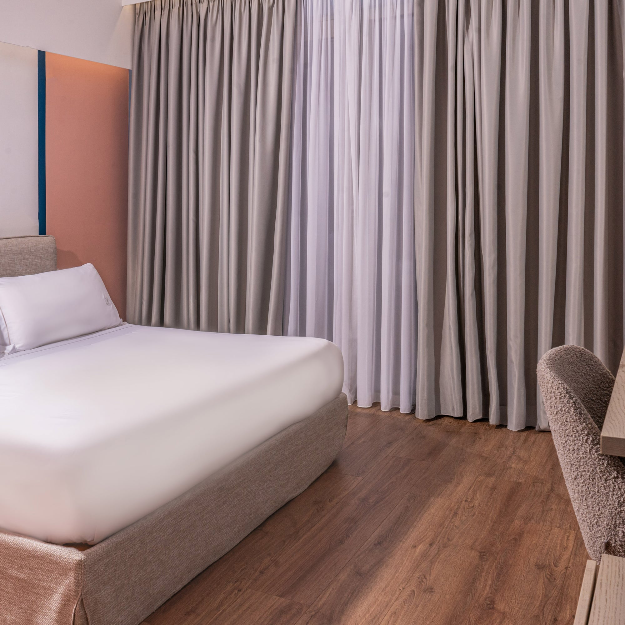Modern hotel room with king bed, color-block wall, hardwood floor, and desk.