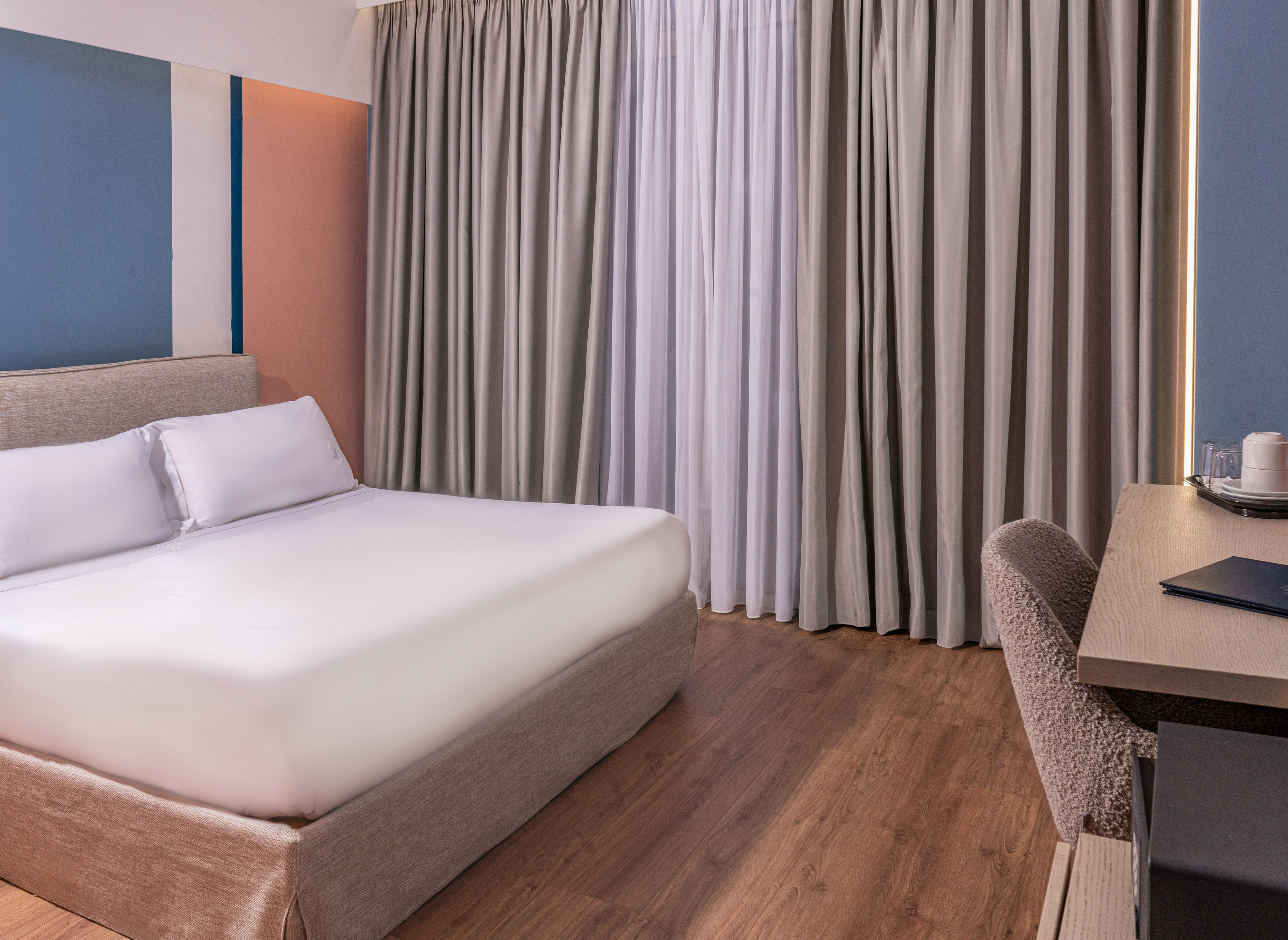 Modern hotel room with king bed, color-block wall, hardwood floor, and desk.