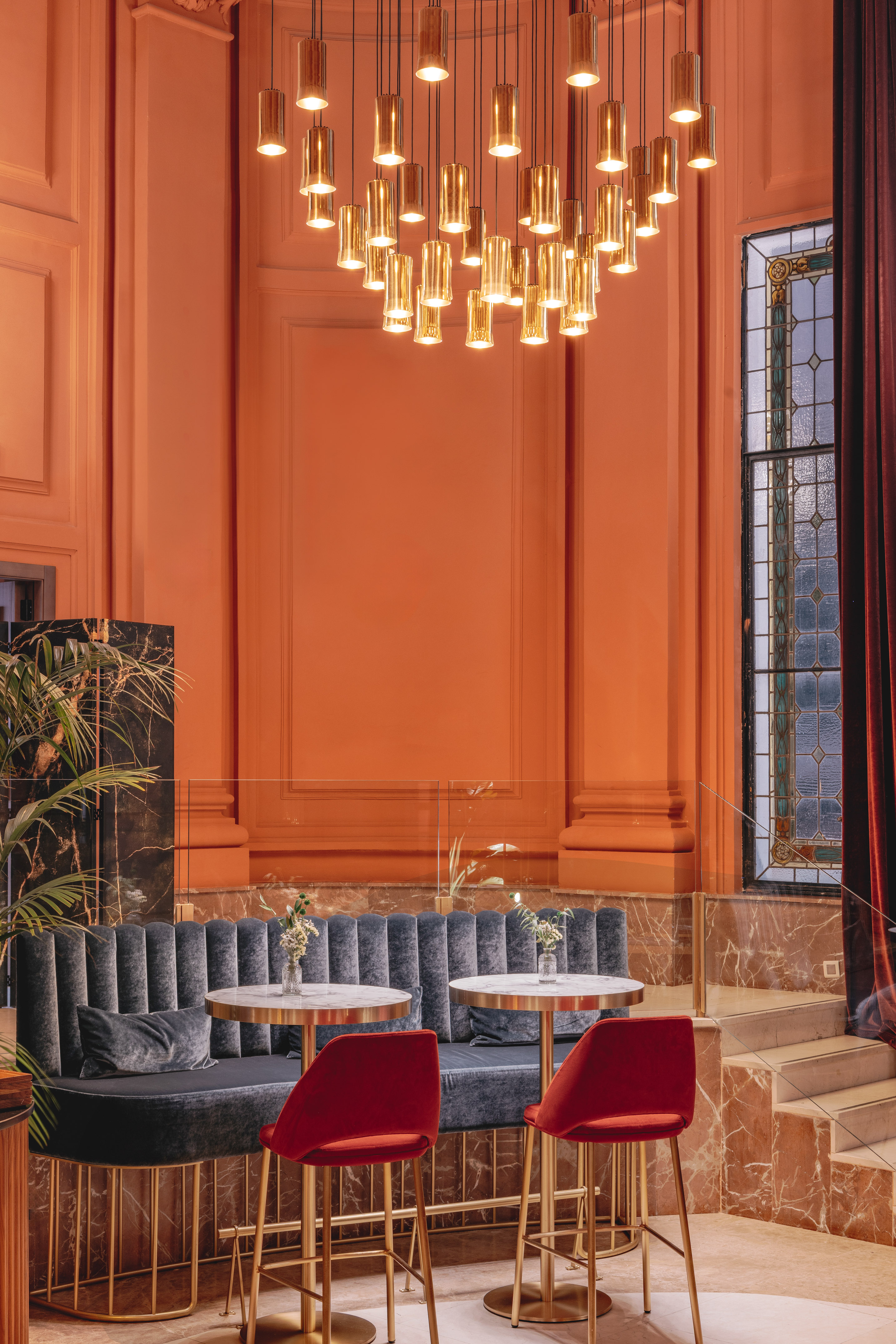 Orange lounge with modern brass chandelier, velvet seating, and marble tables.
