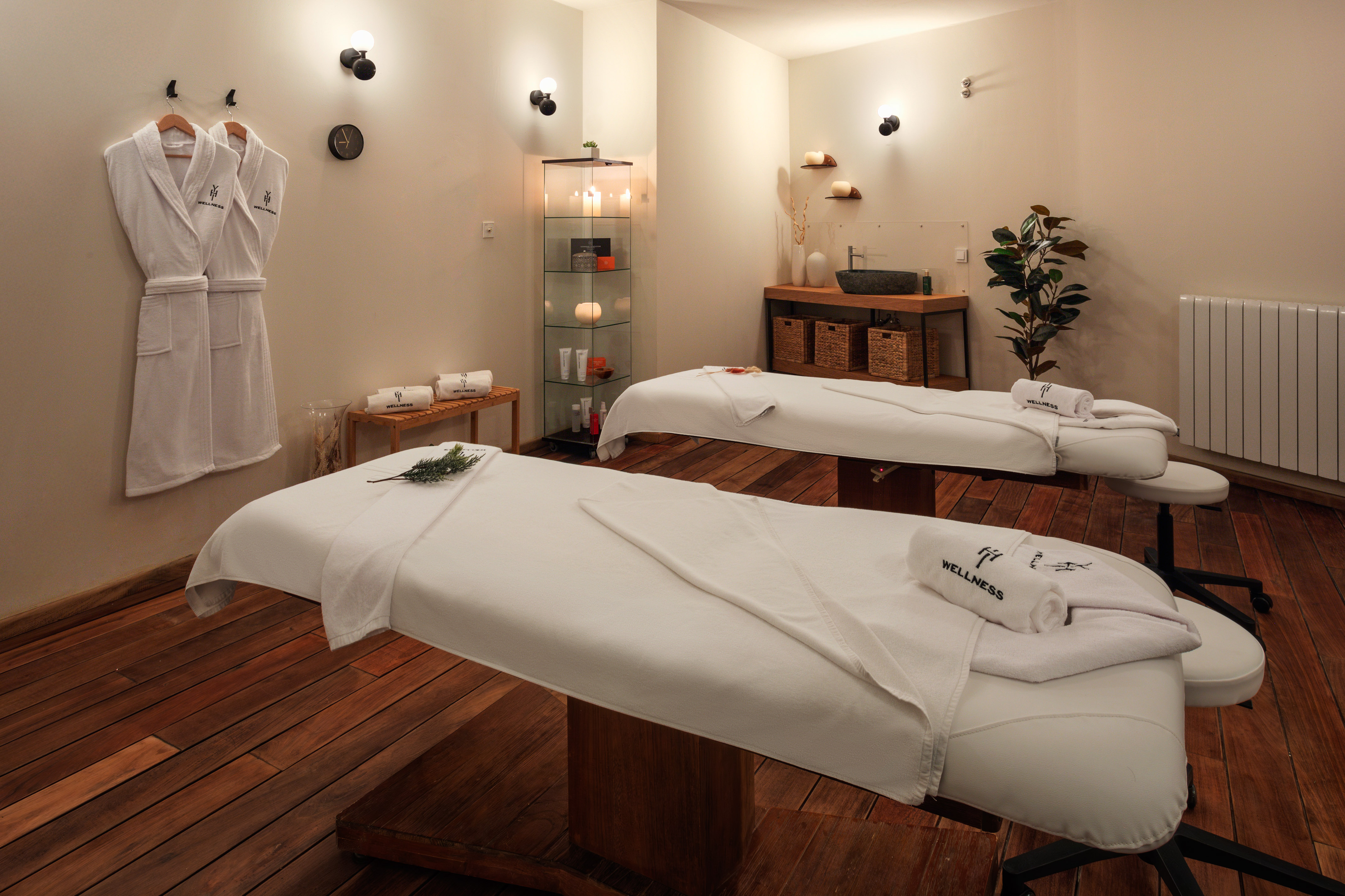 Spa massage room with two treatment tables, bathrobes, and wellness towels.