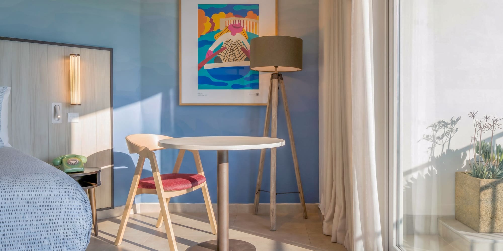 Modern hotel room: blue wall, abstract art, sitting area, and balcony.