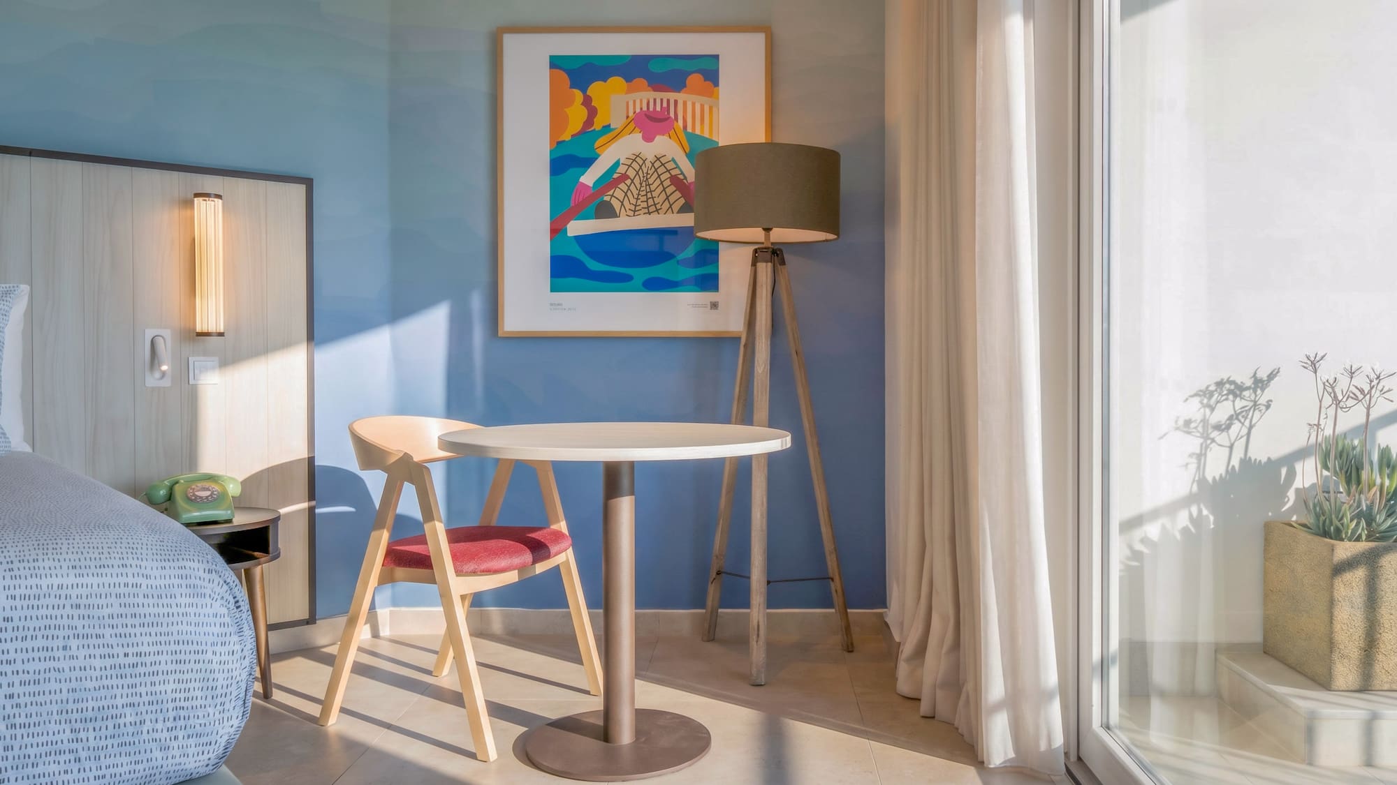 Modern hotel room: blue wall, abstract art, sitting area, and balcony.