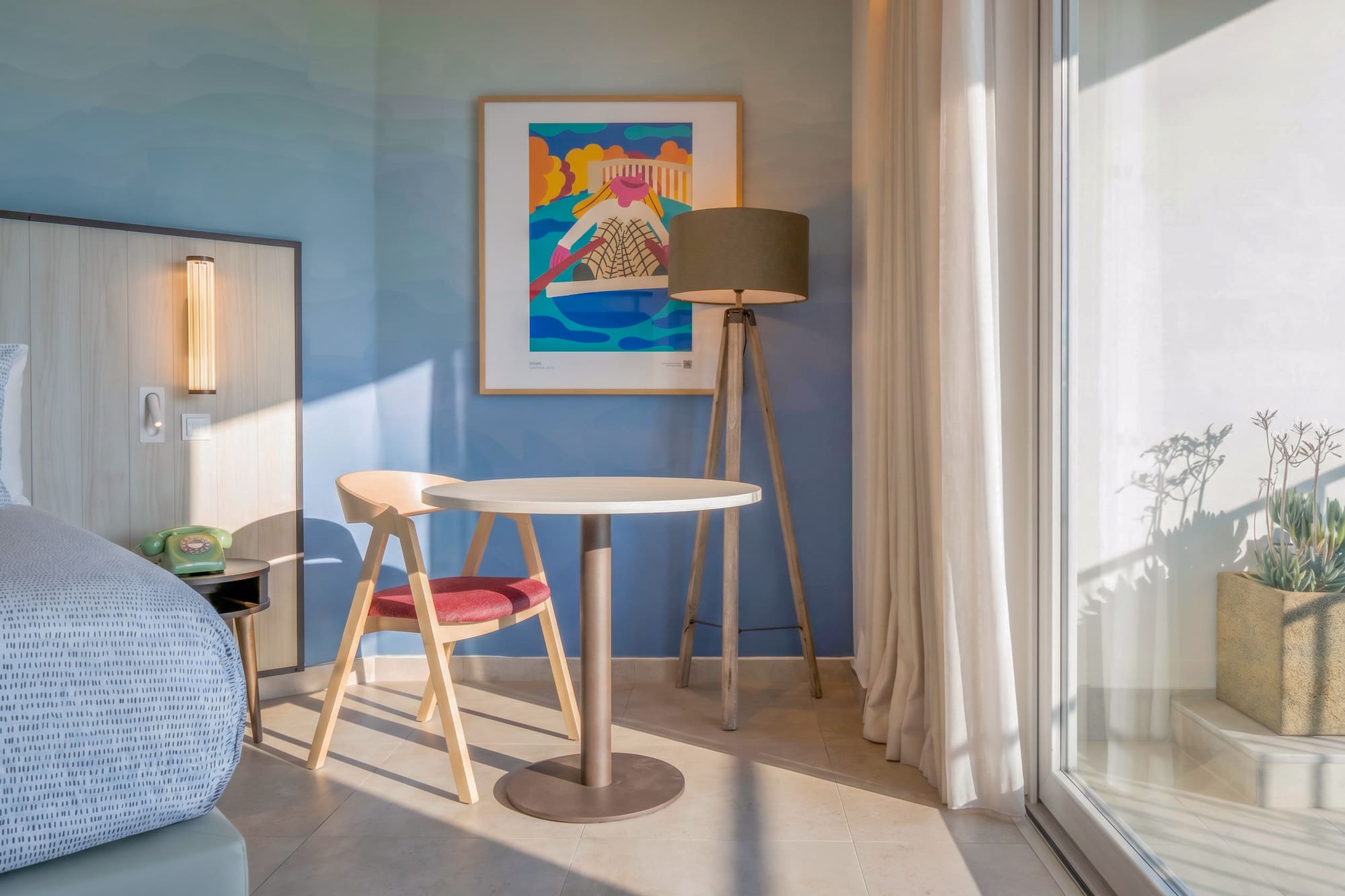 Modern hotel room: blue wall, abstract art, sitting area, and balcony.