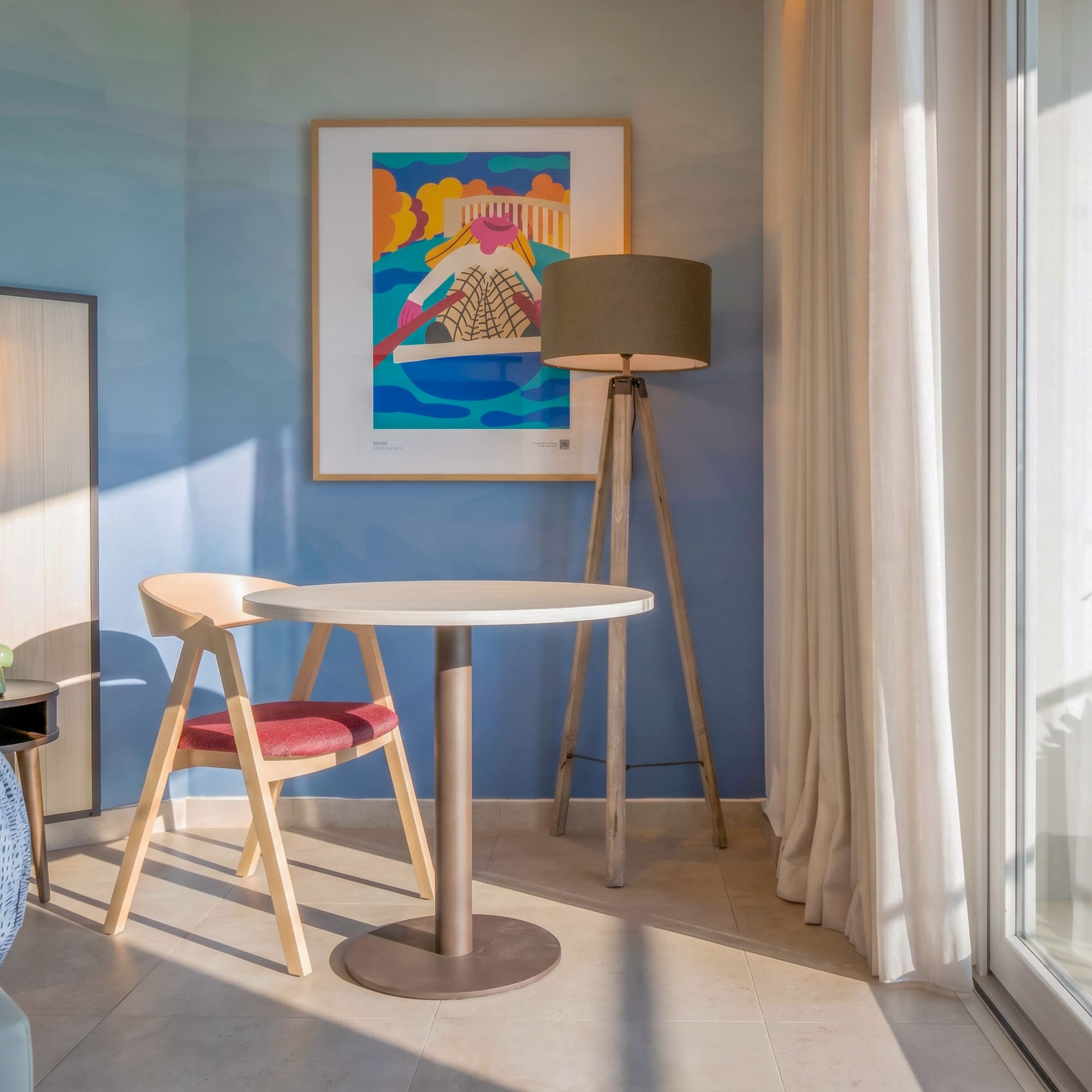 Modern hotel room: blue wall, abstract art, sitting area, and balcony.
