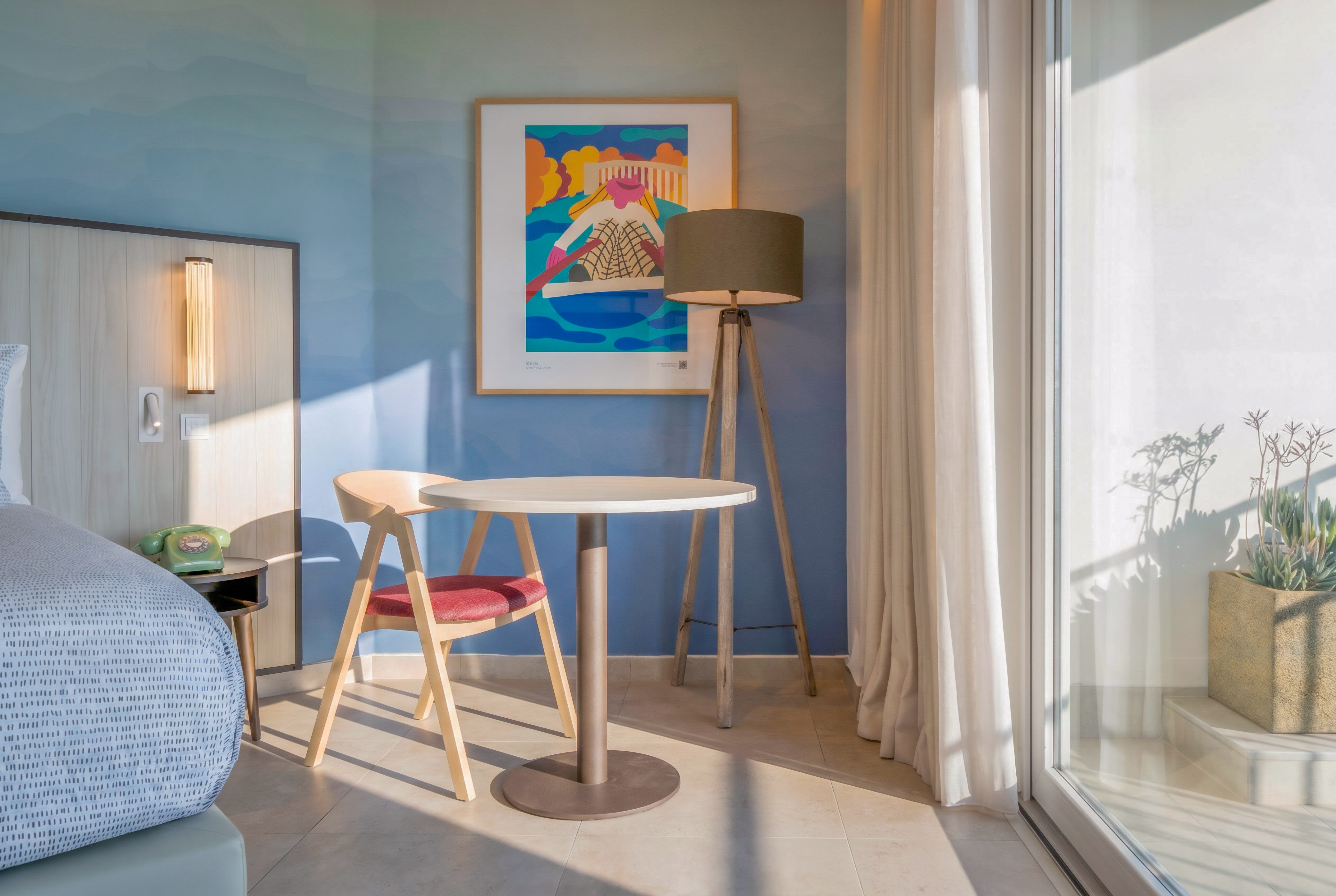 Modern hotel room: blue wall, abstract art, sitting area, and balcony.
