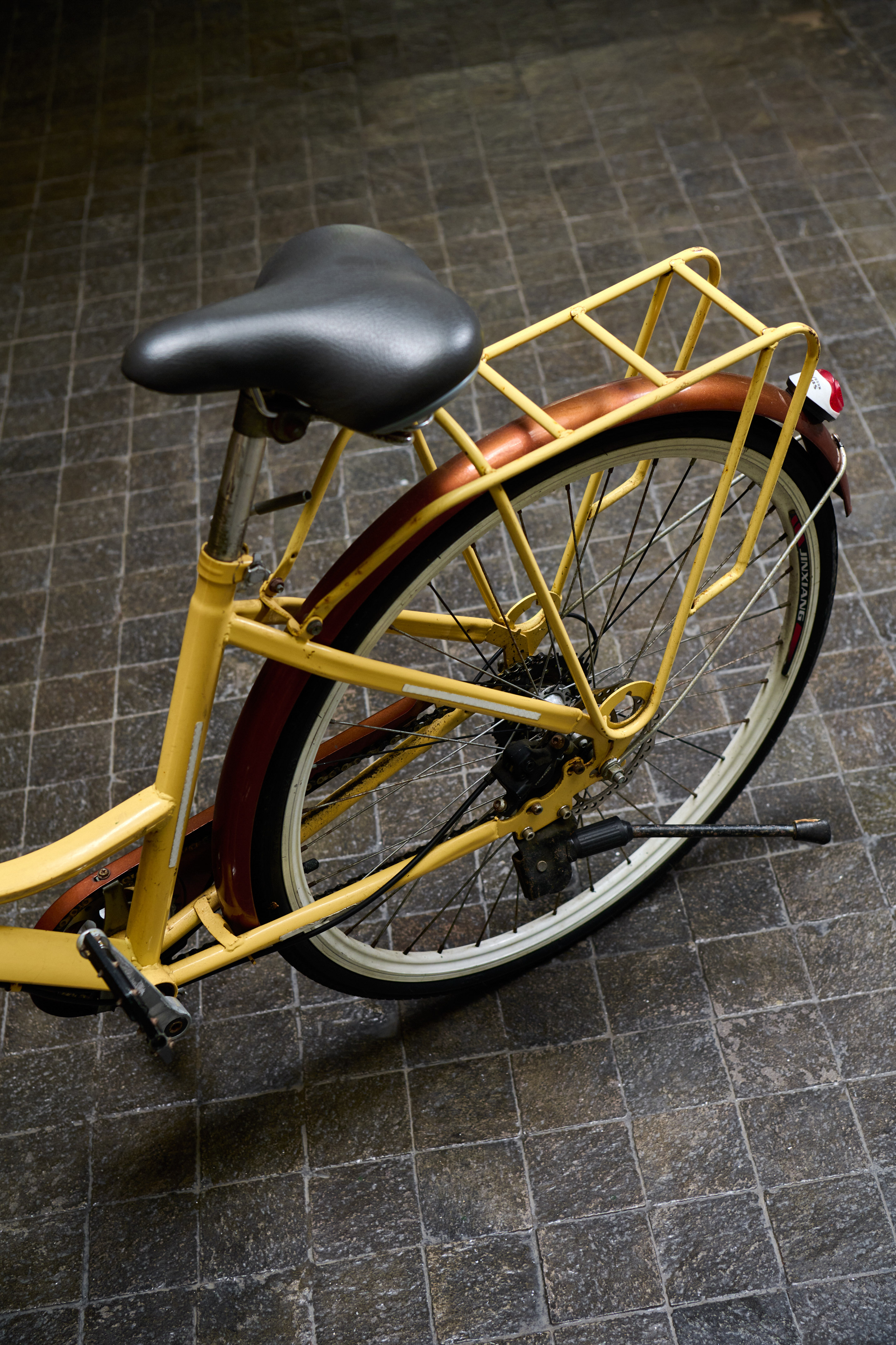 Yellow bicycle with black seat, brown fender, and rear rack on pavement.