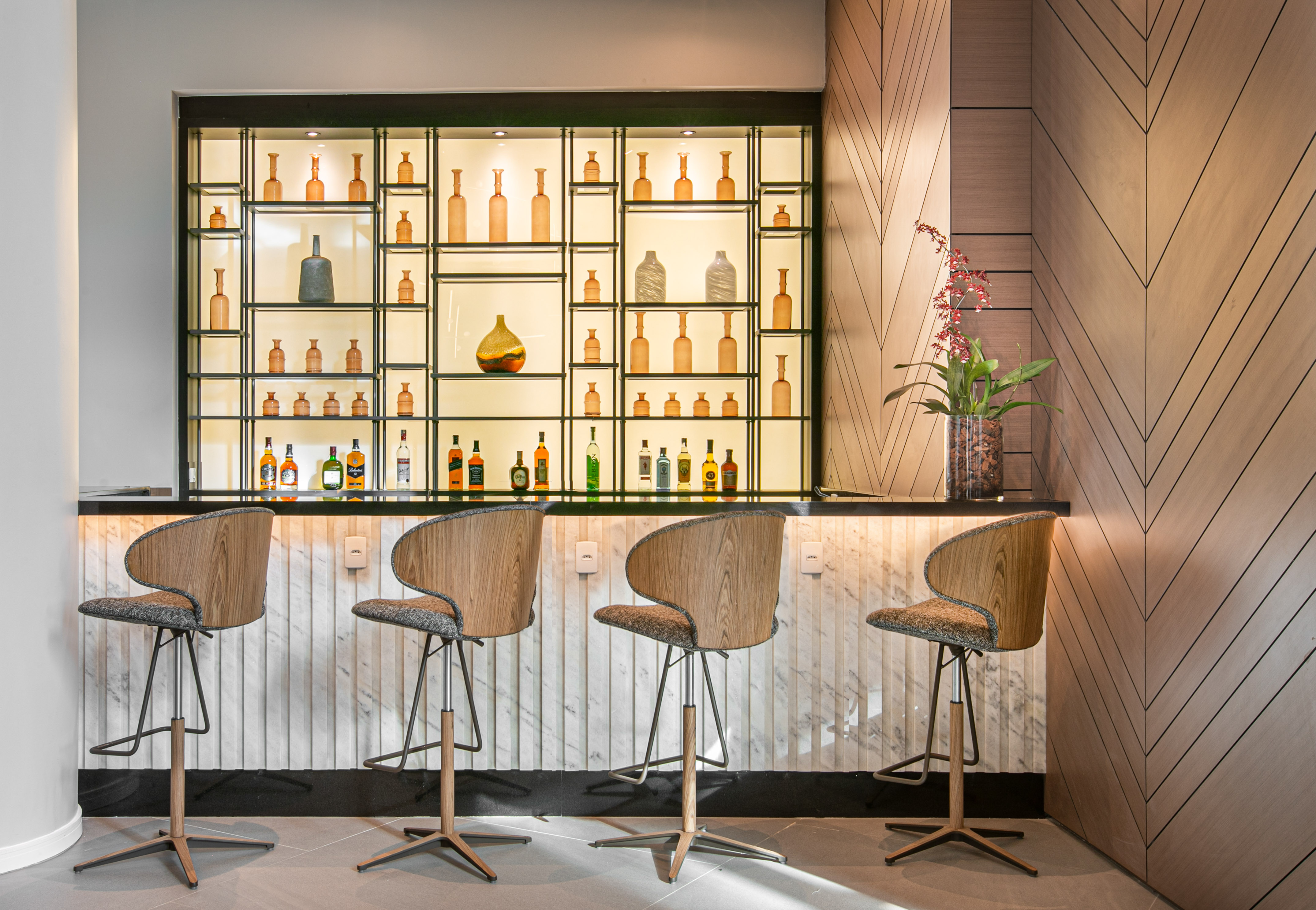 Modern hotel bar interior with backlit liquor display and four bar stools.