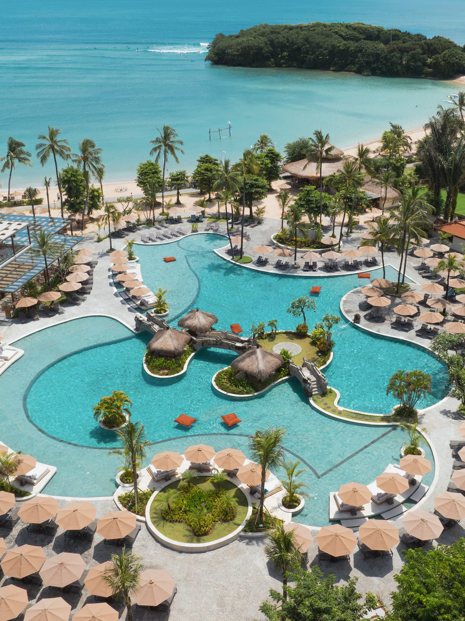 Luxury tropical resort pool, palm trees, sandy beach, and turquoise ocean.