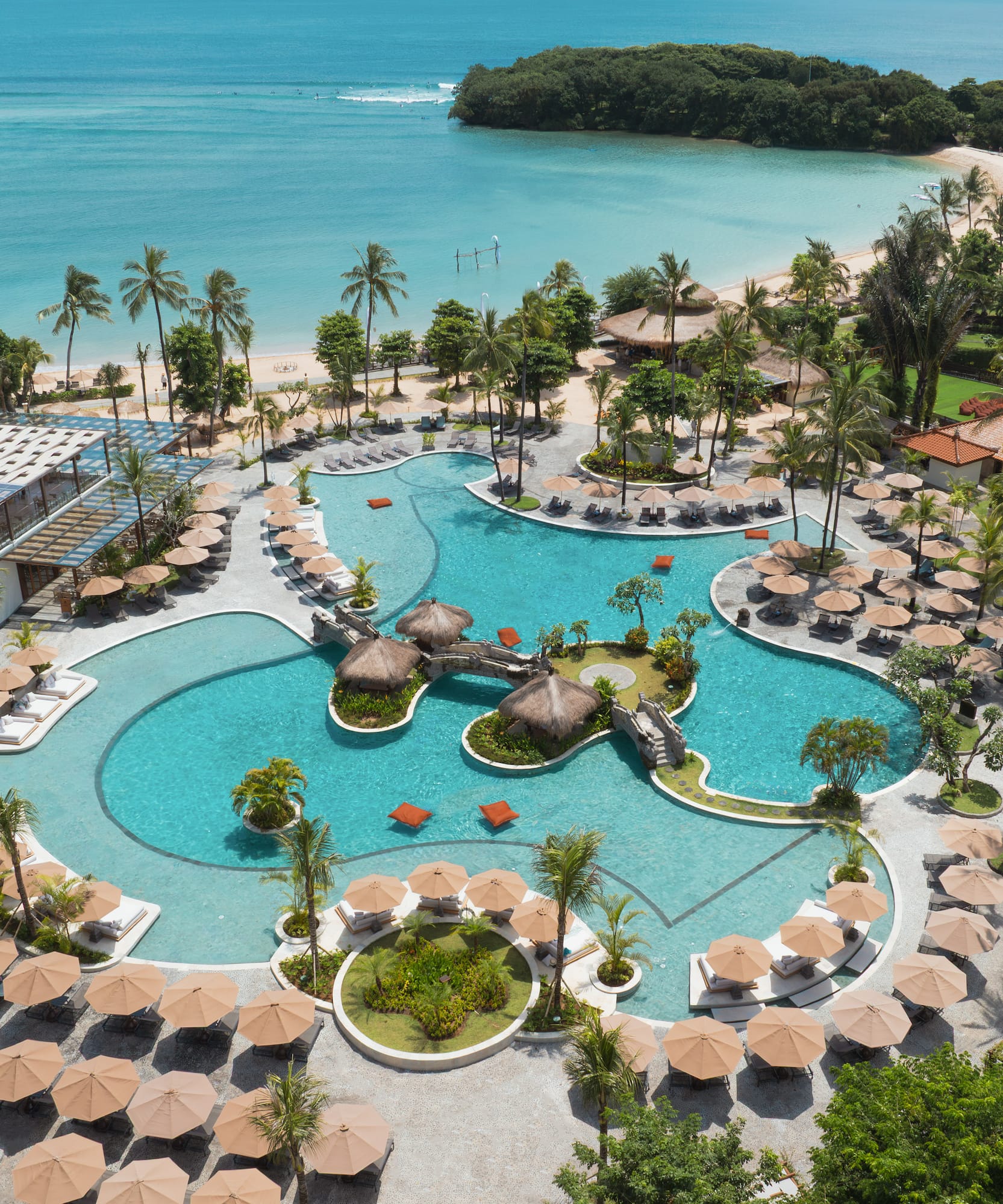Luxury tropical resort pool, palm trees, sandy beach, and turquoise ocean.