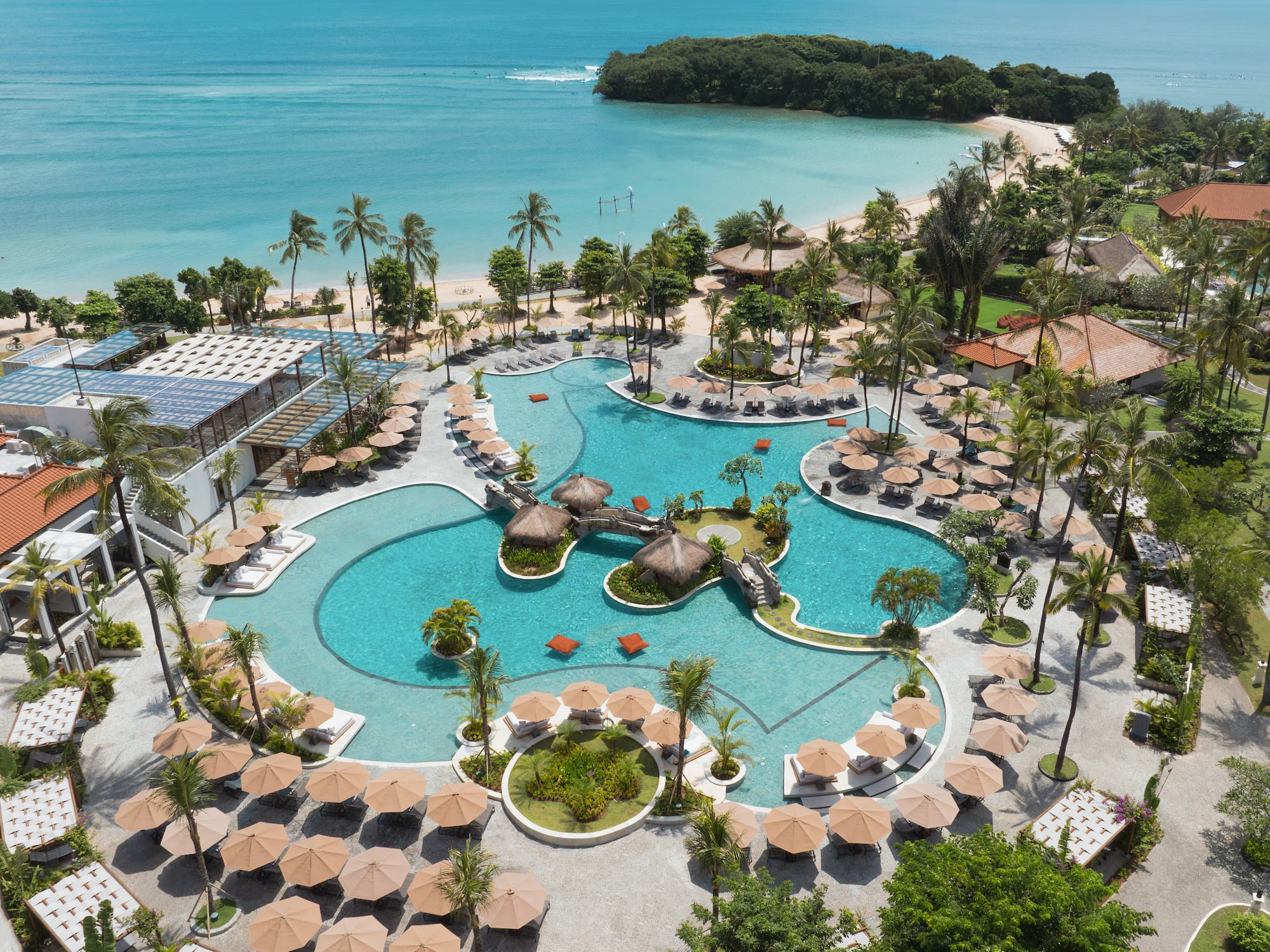 Luxury tropical resort pool, palm trees, sandy beach, and turquoise ocean.