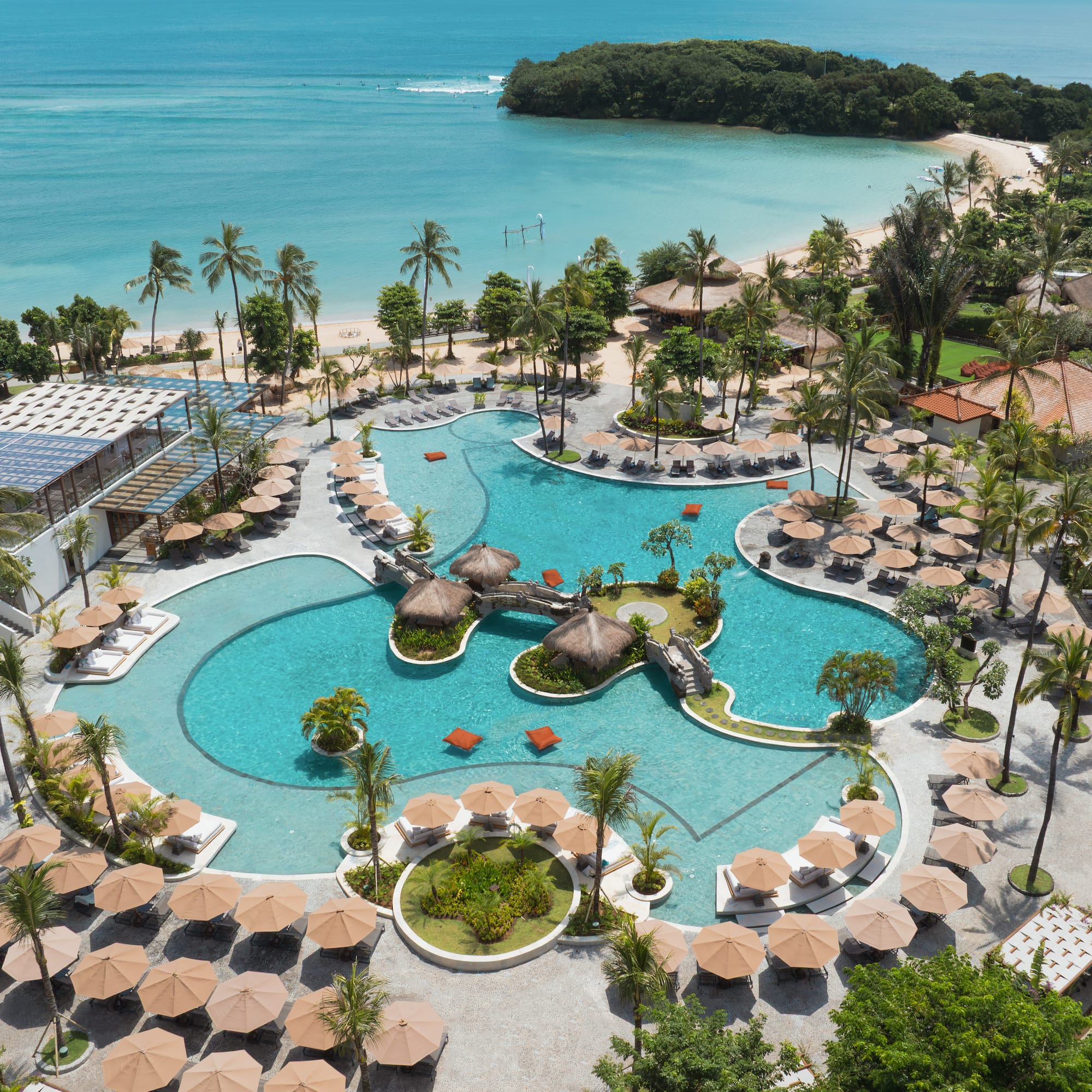 Luxury tropical resort pool, palm trees, sandy beach, and turquoise ocean.