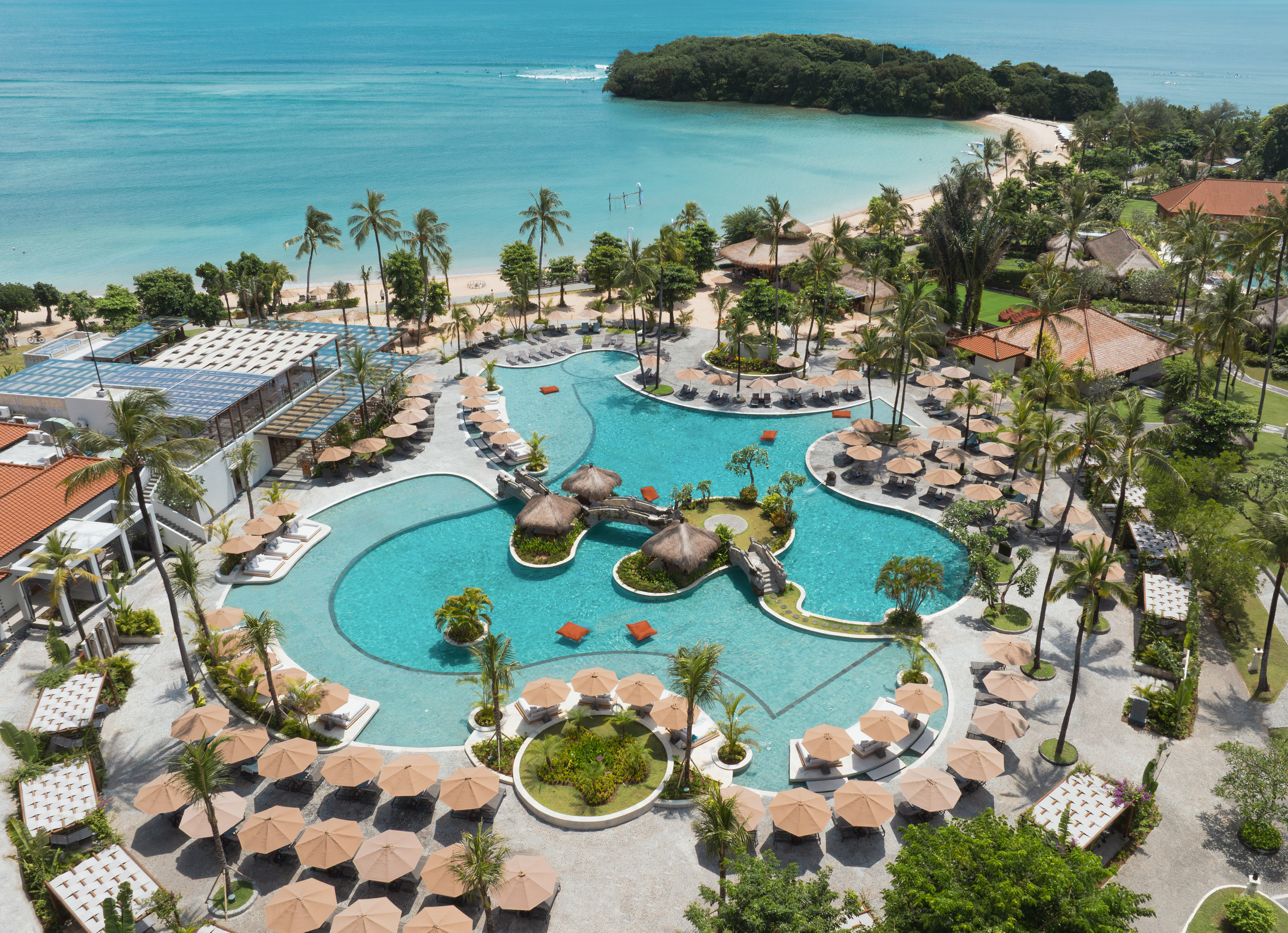 Luxury tropical resort pool, palm trees, sandy beach, and turquoise ocean.