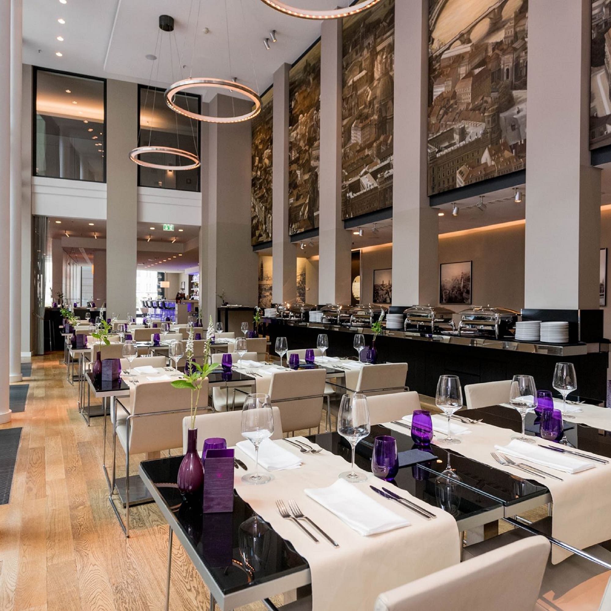 Modern restaurant dining room with elegant table settings, city murals, and buffet.