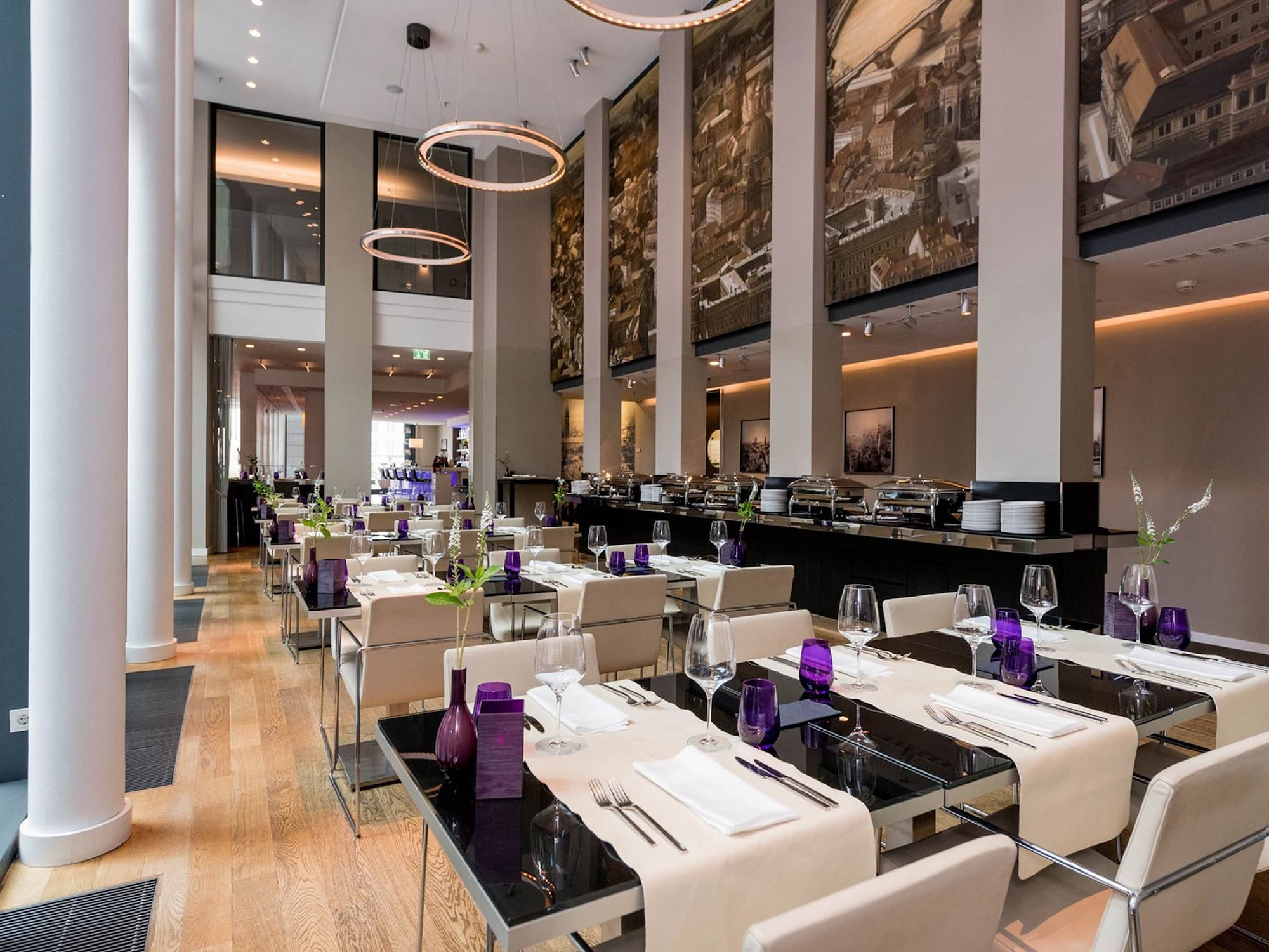 Modern hotel restaurant interior with set tables, buffet, and cityscape murals.