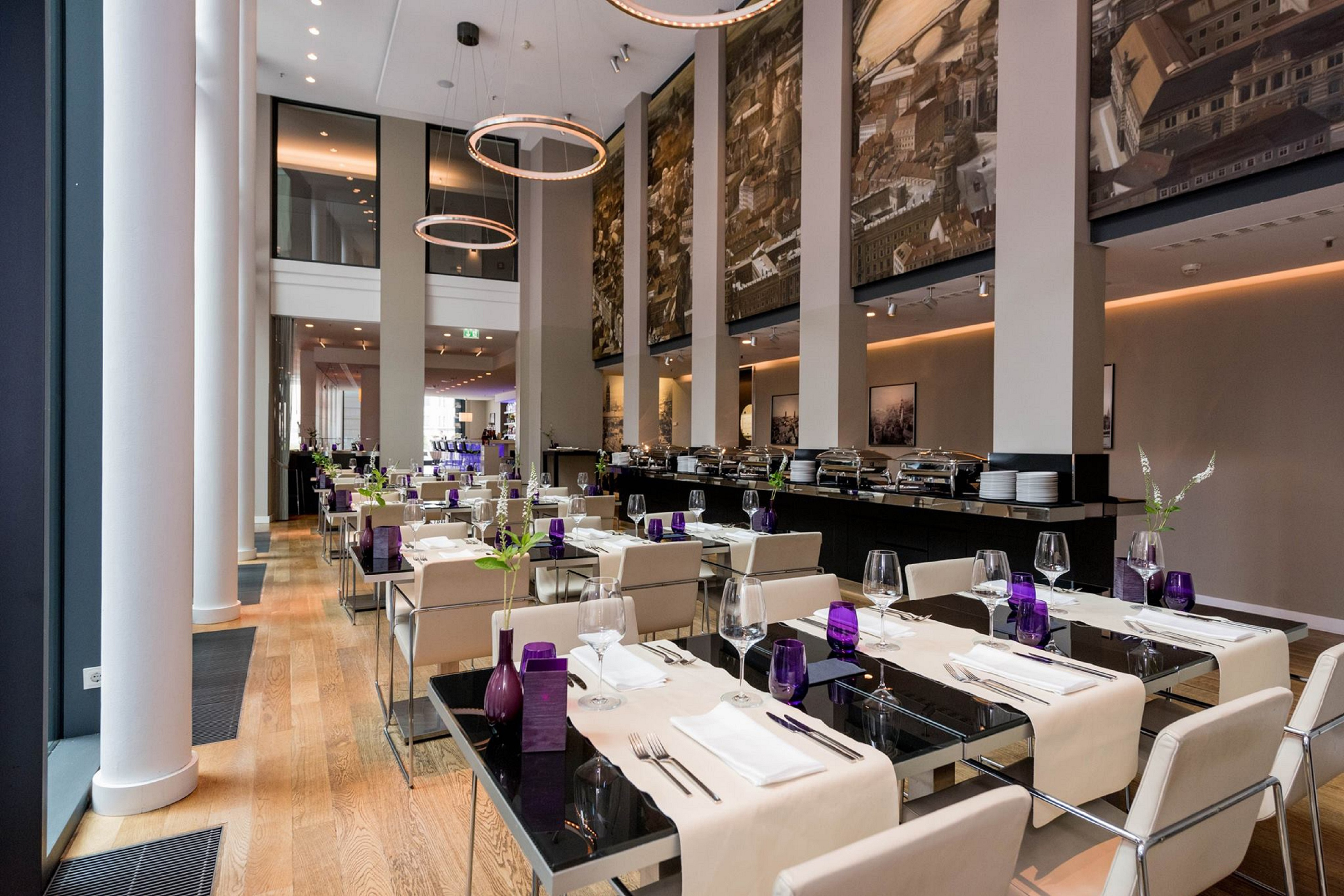 Modern hotel restaurant interior with set tables, buffet, and cityscape murals.