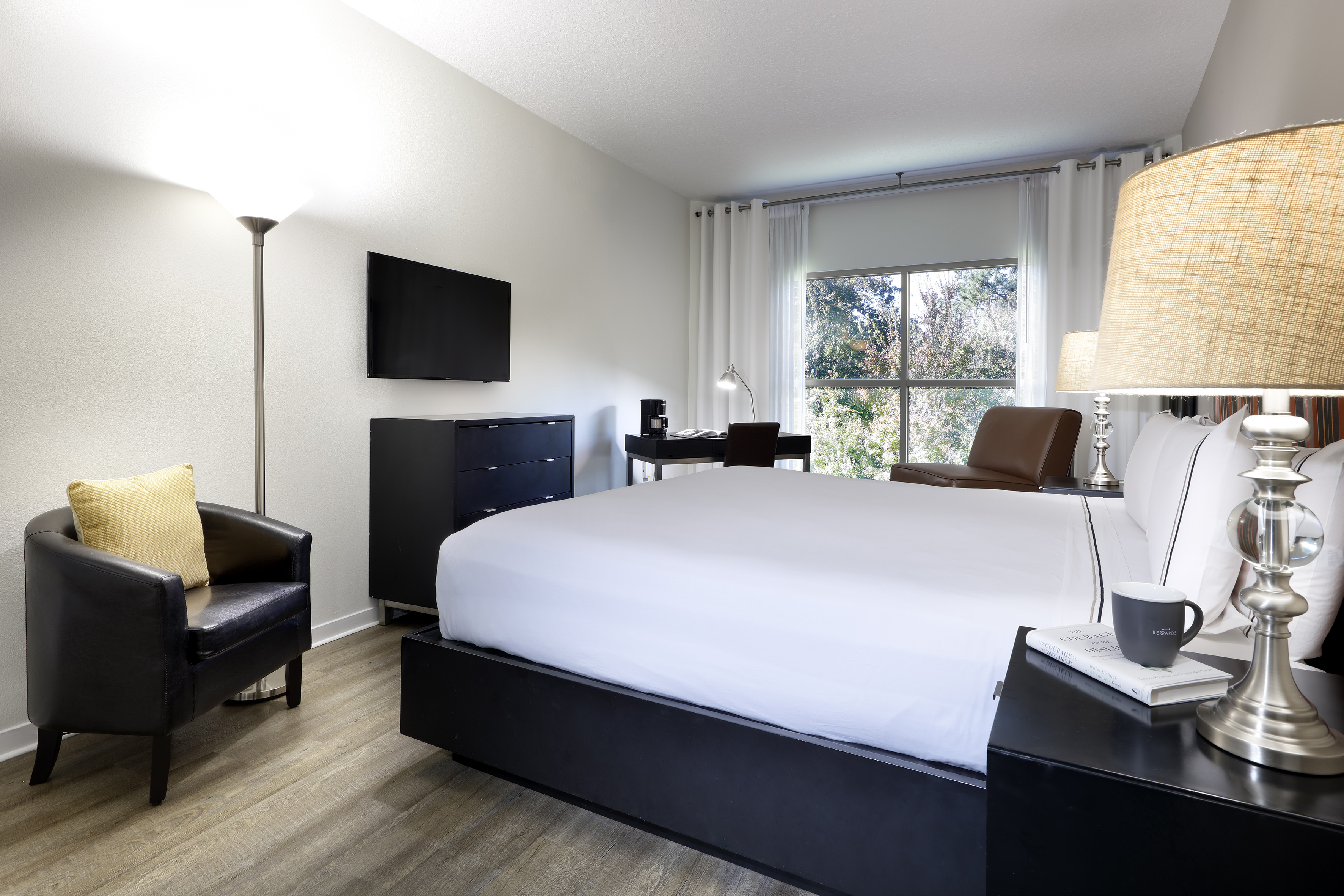 Modern hotel bedroom with king bed, workstation, TV, and large window.