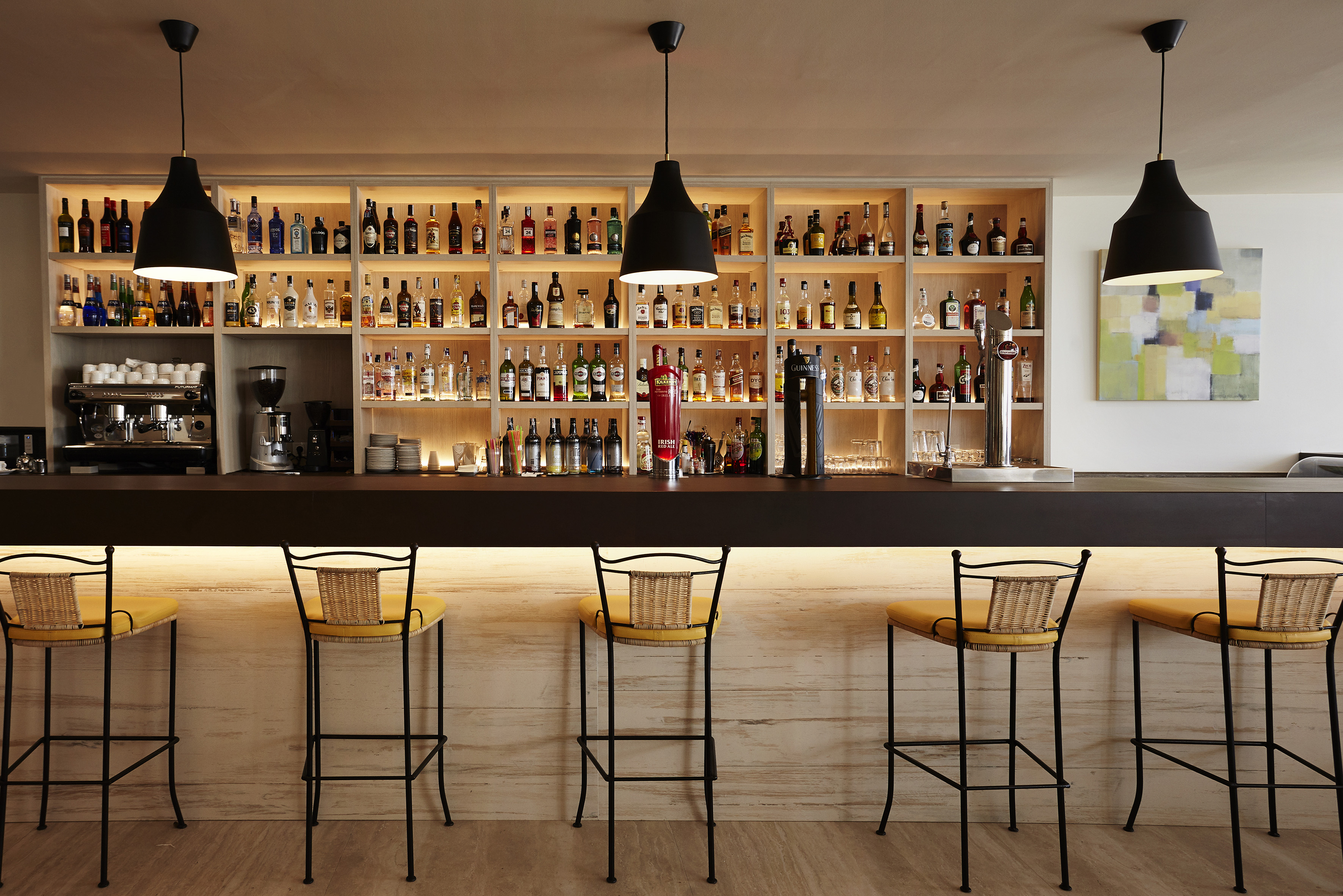 Modern cocktail bar with backlit liquor bottles and yellow bar stools.