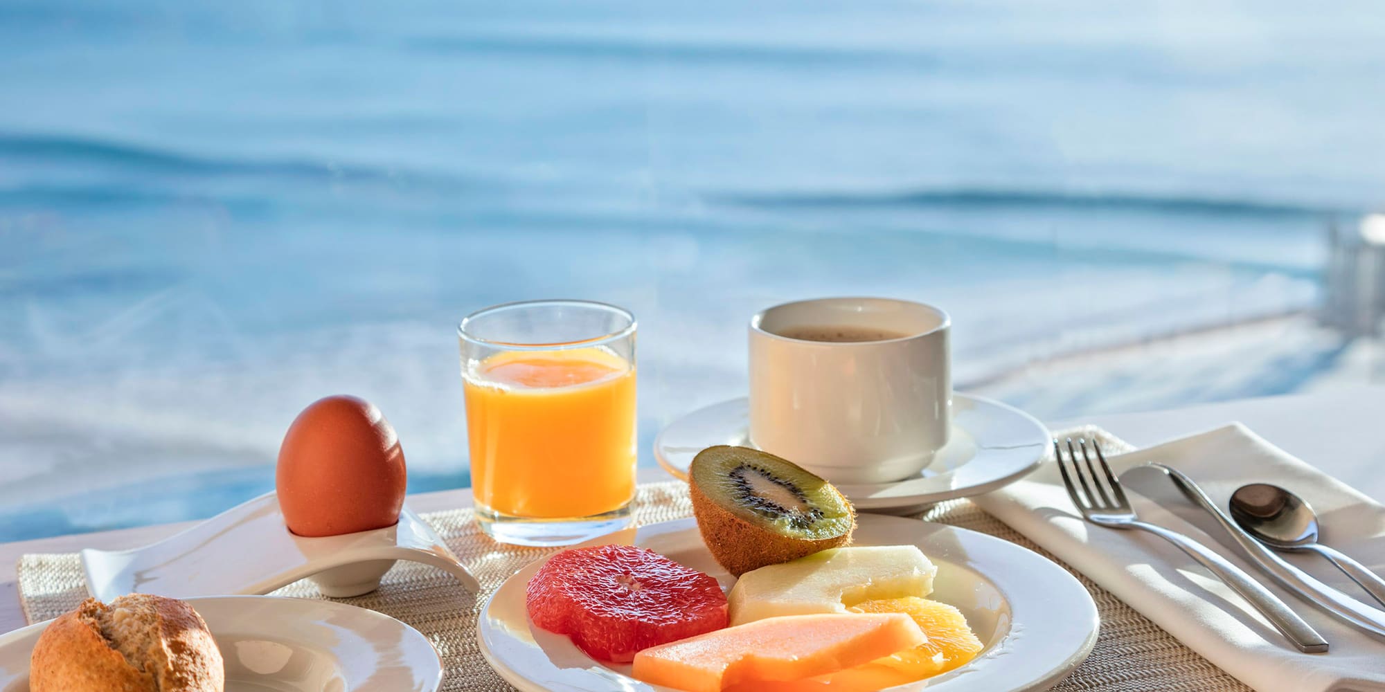 a plate of fruit and a egg on a table with a body of water