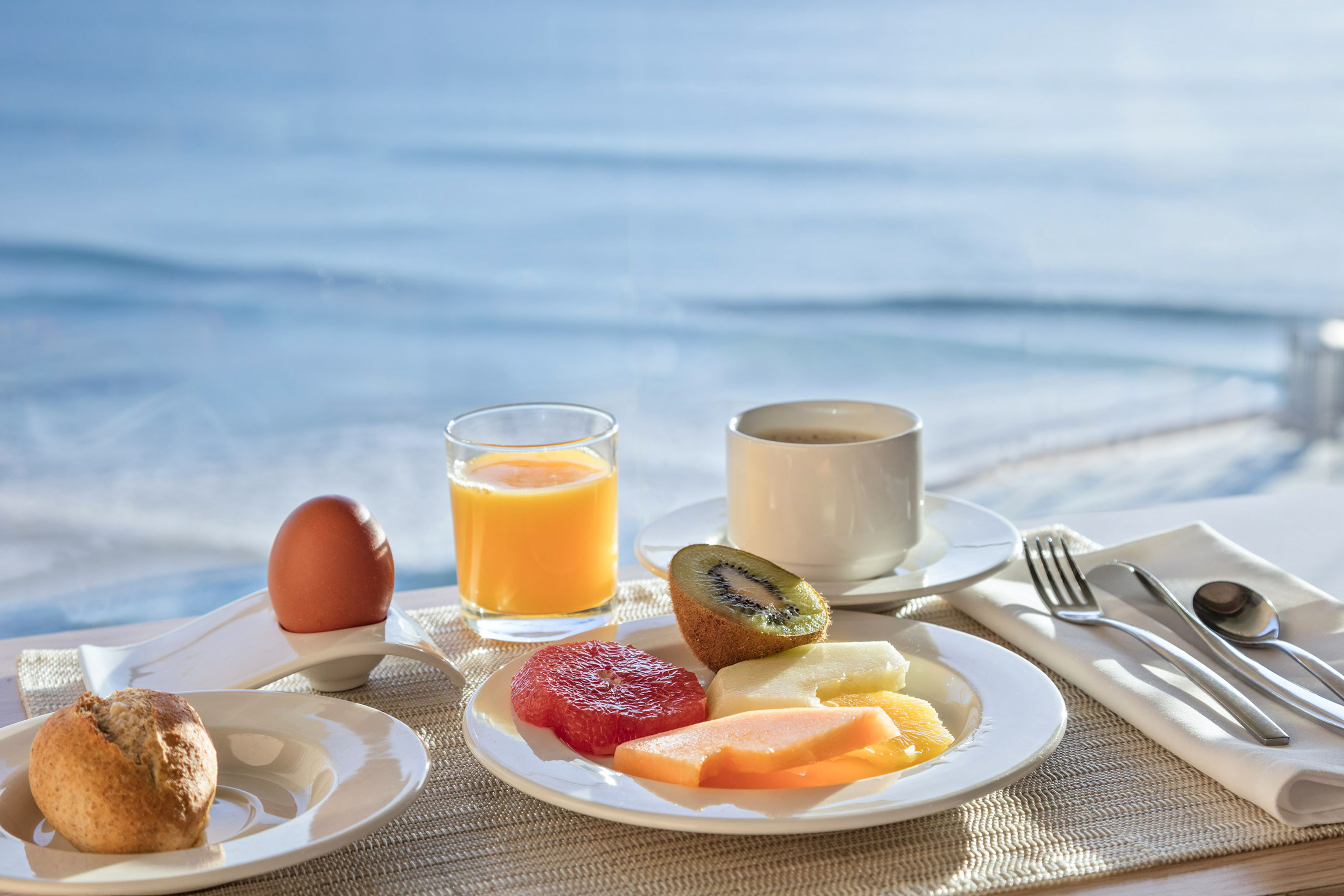 Breakfast by the ocean with fresh fruit, coffee, juice, egg, and bread roll.