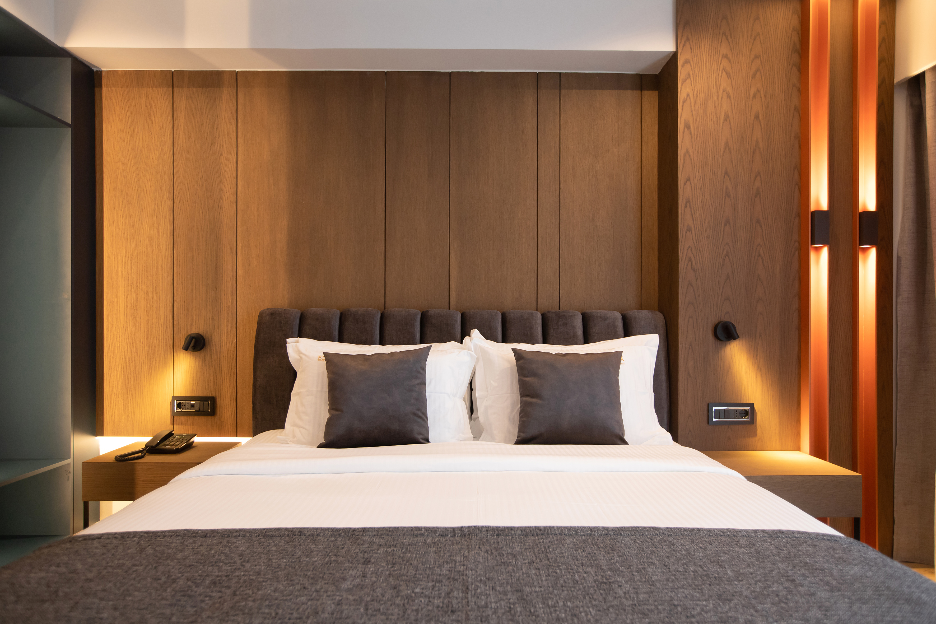 Modern hotel bedroom with wooden headboard, white bed, and accent lighting.