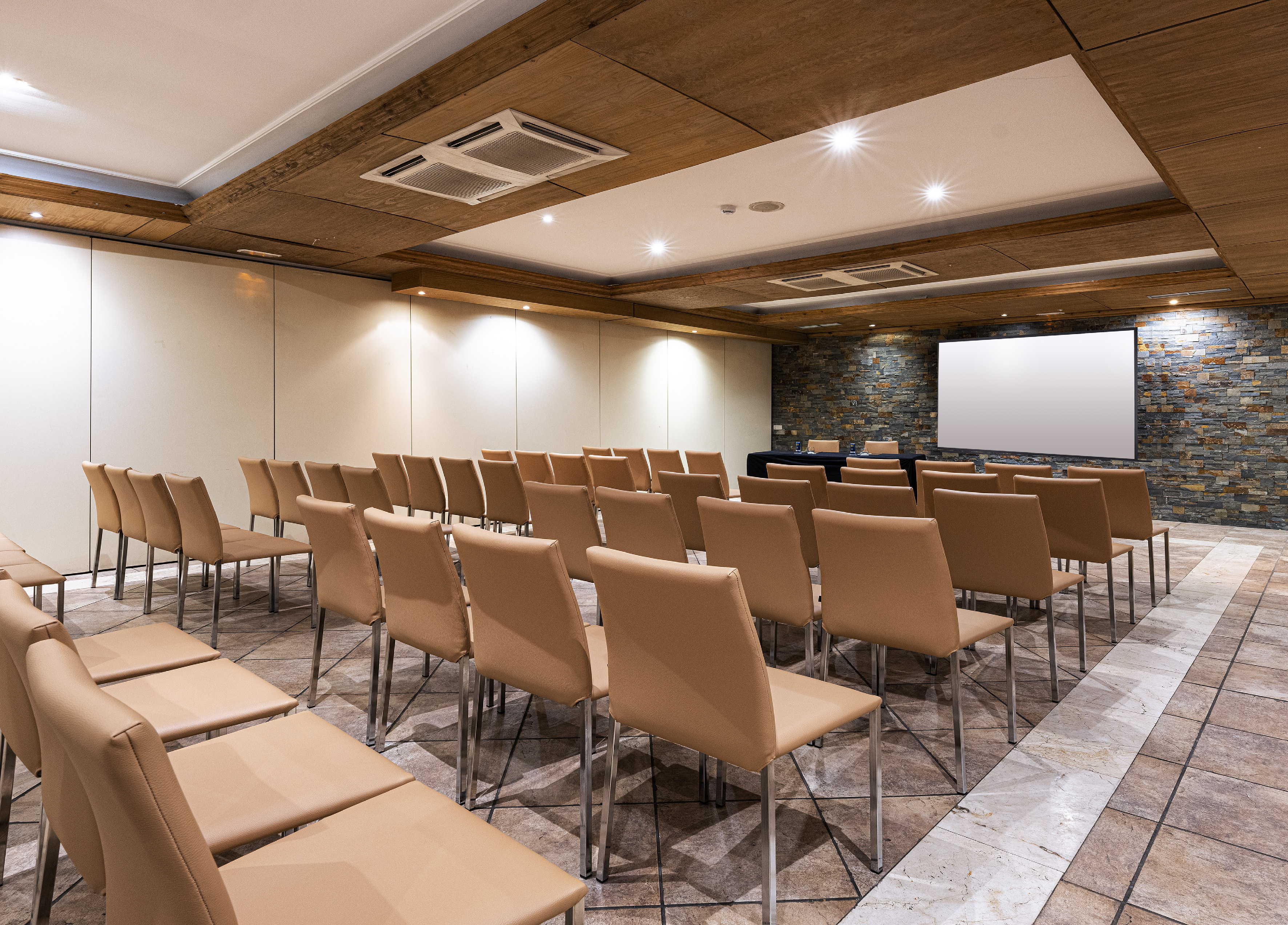 Conference room with beige chairs, projection screen, stone wall, and wood ceiling.