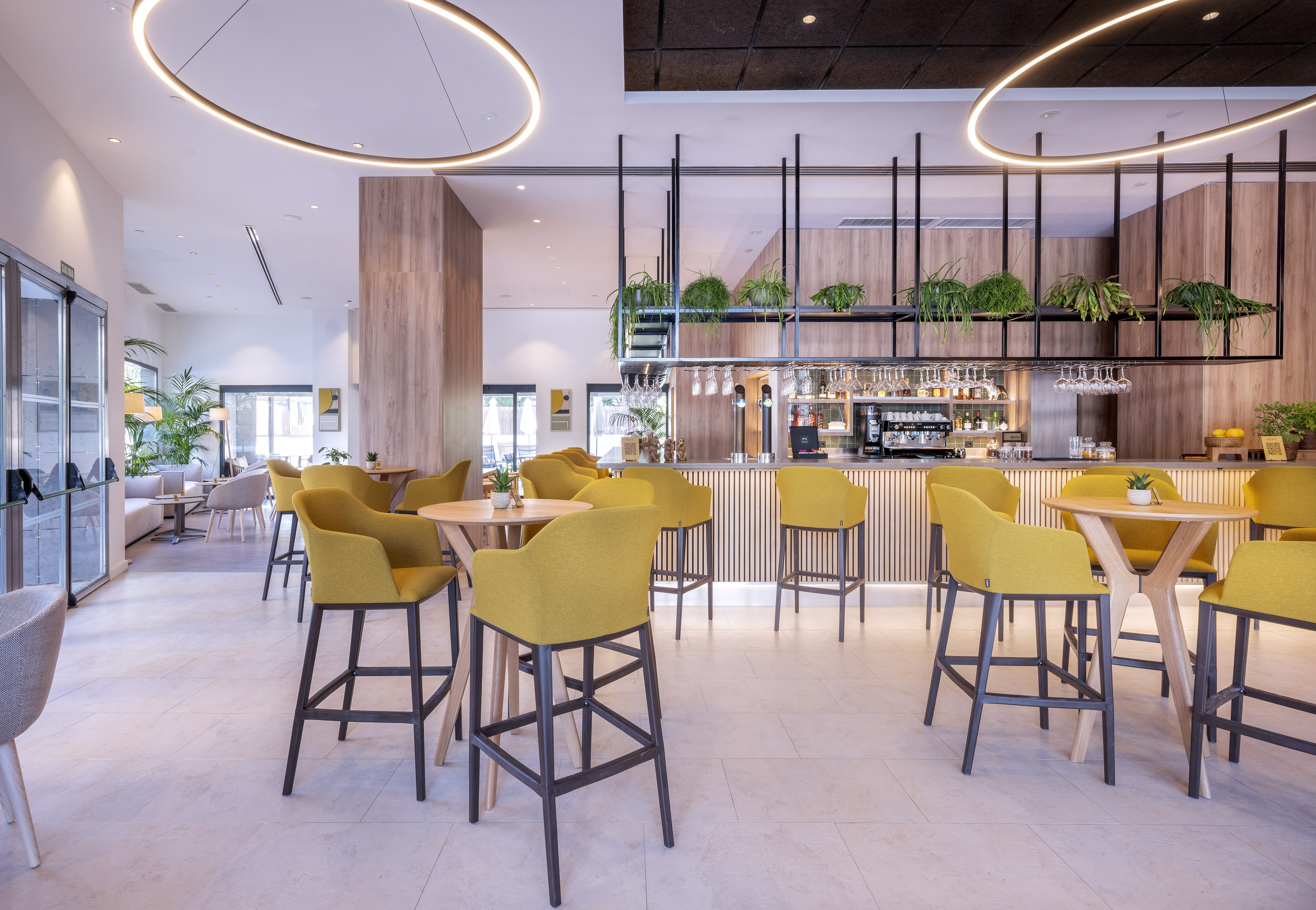 Modern hotel bar lounge with yellow chairs, wooden tables, and bar counter.