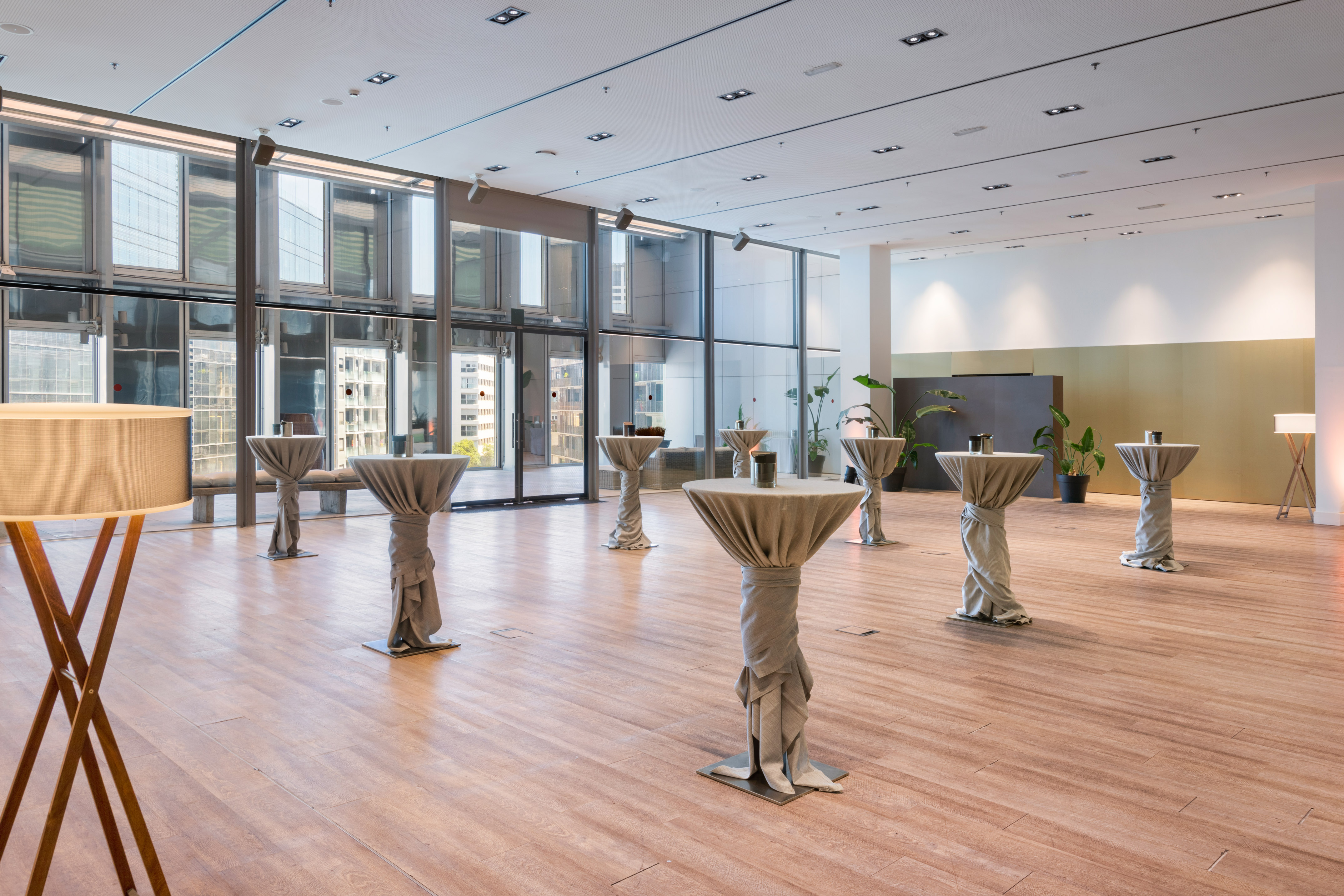 Modern reception room with grey draped cocktail tables, wood floor, city view.