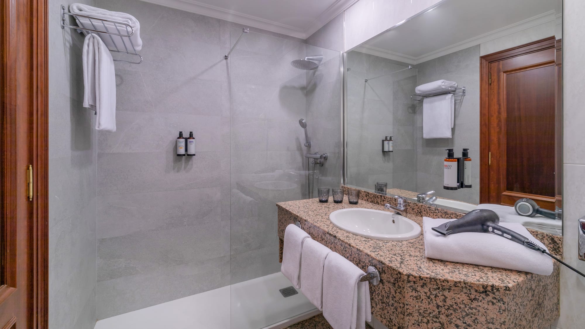 Bright hotel bathroom with granite vanity, sink, walk-in shower, and hairdryer.