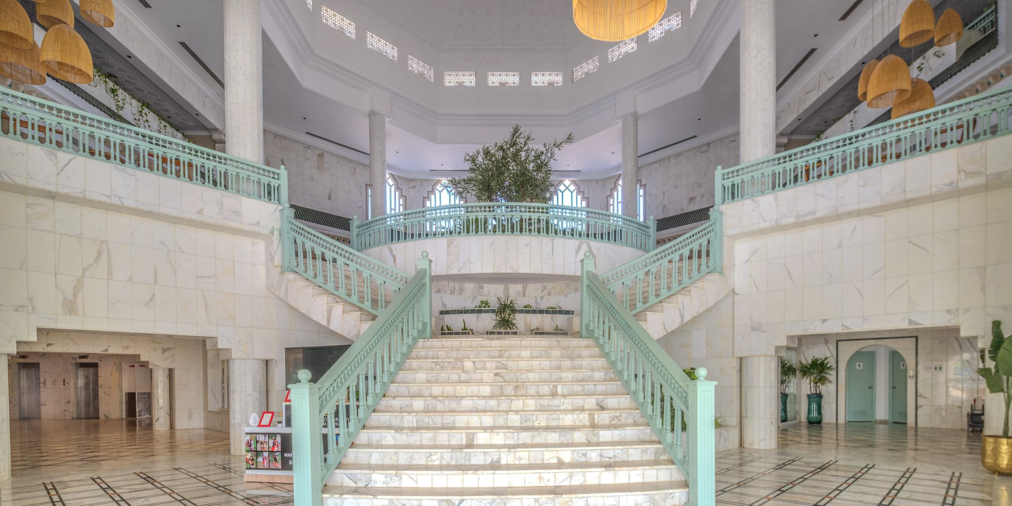 Grand hotel atrium with marble staircase and mint green railings.